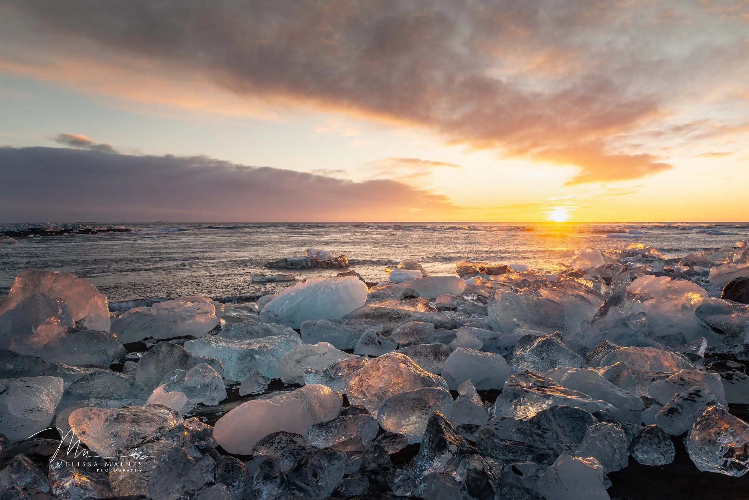 Sunrise at Diamond Beach in southern Iceland with a shoreline covered in large ice chunks.