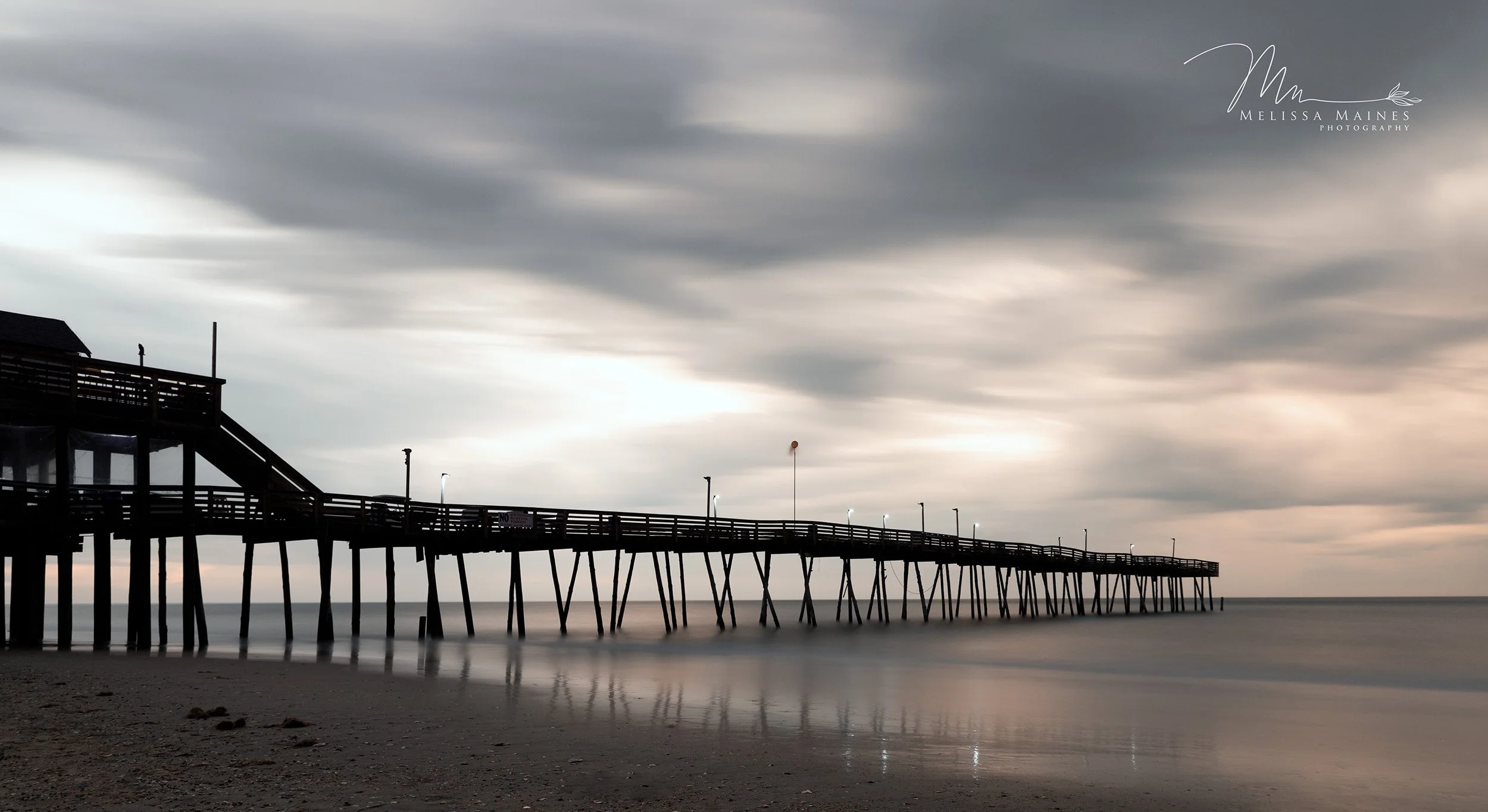 Long exposure photograph of a wooden pier extending over calm ocean water near Outer Banks.