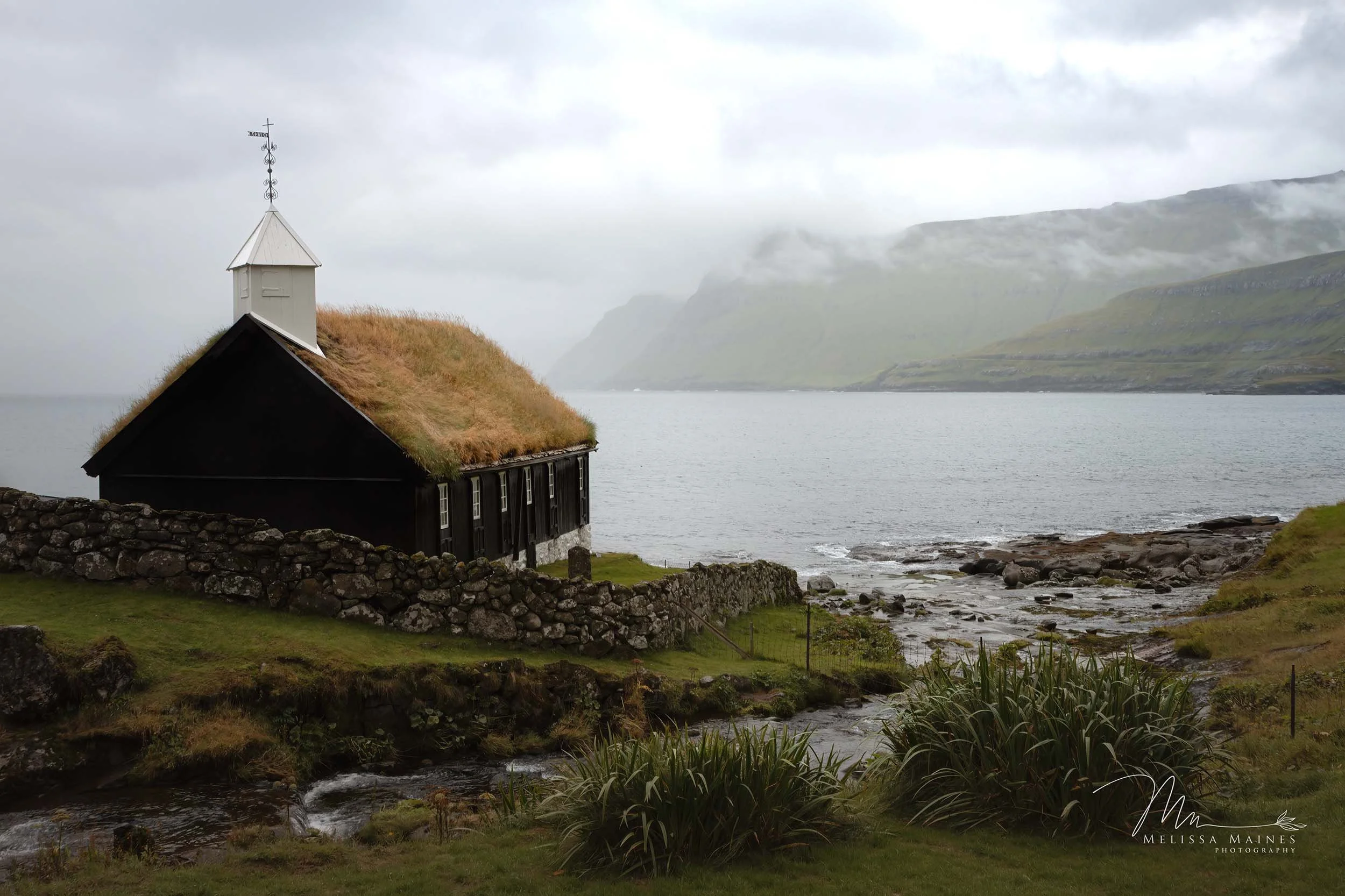 Black Church, Fuglafjordbur, Faroe Islands featuring a grass roof overlooking the sea and mountains.