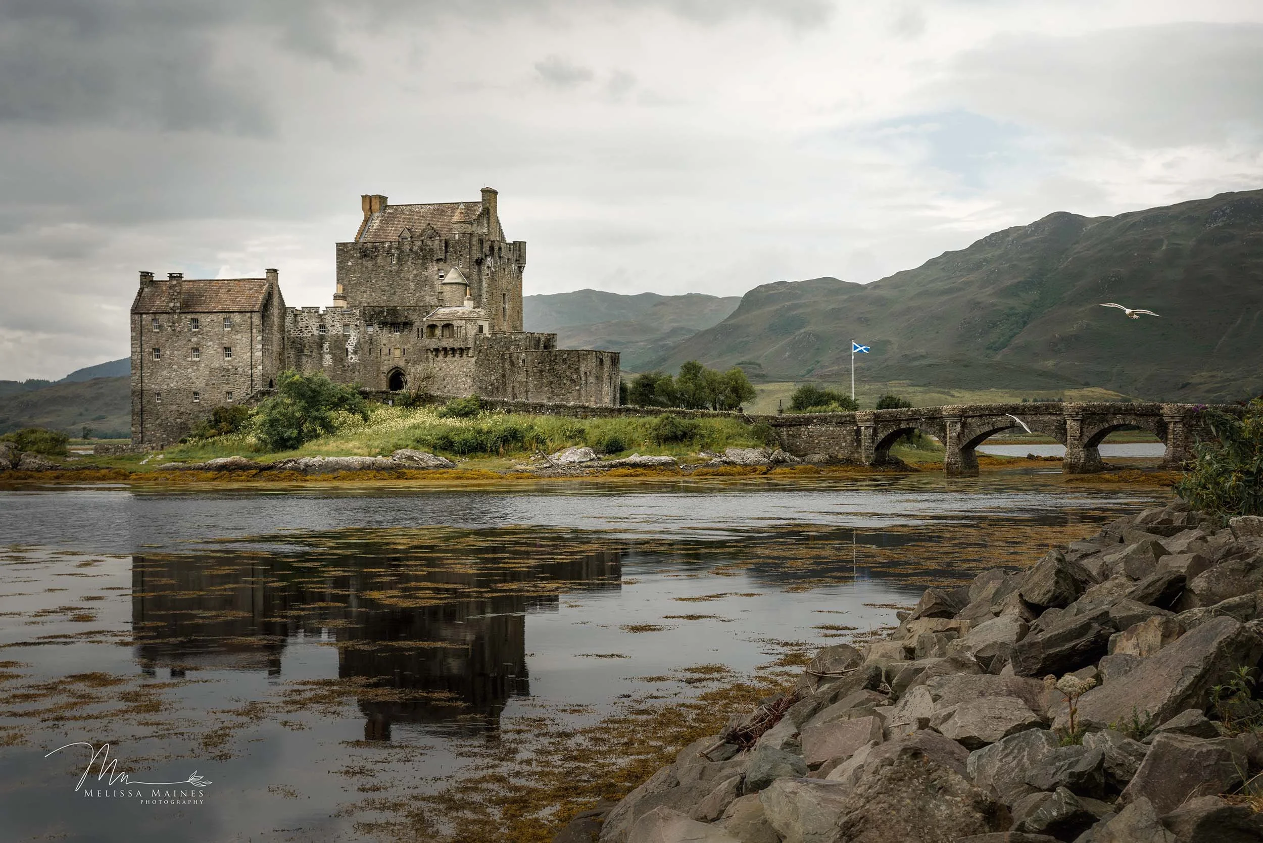The historic stone Eilean Donan castle with a Scottish flag flying nearby.