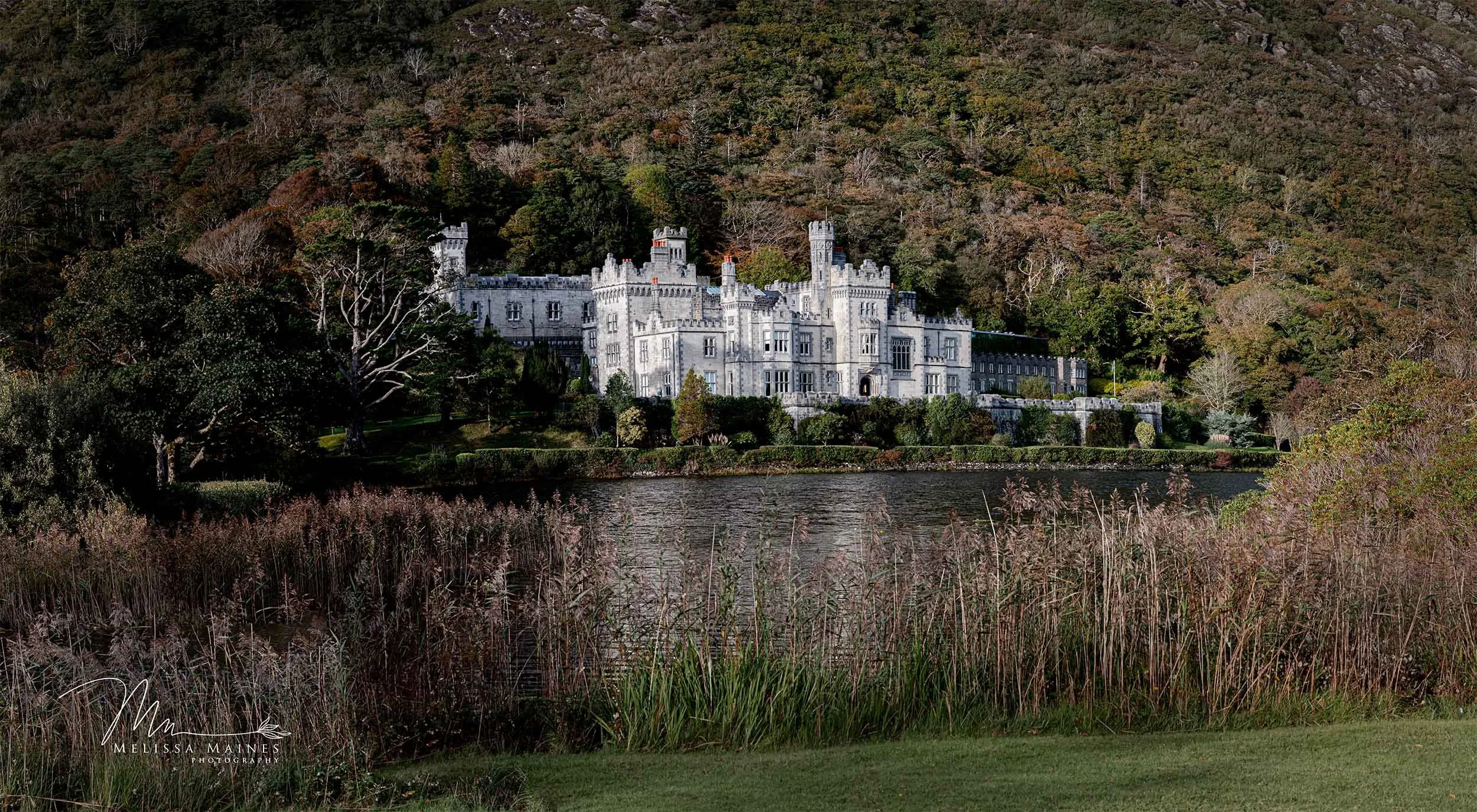 Kylemore Abbey surrounded by trees, situated on the edge of small lake.
