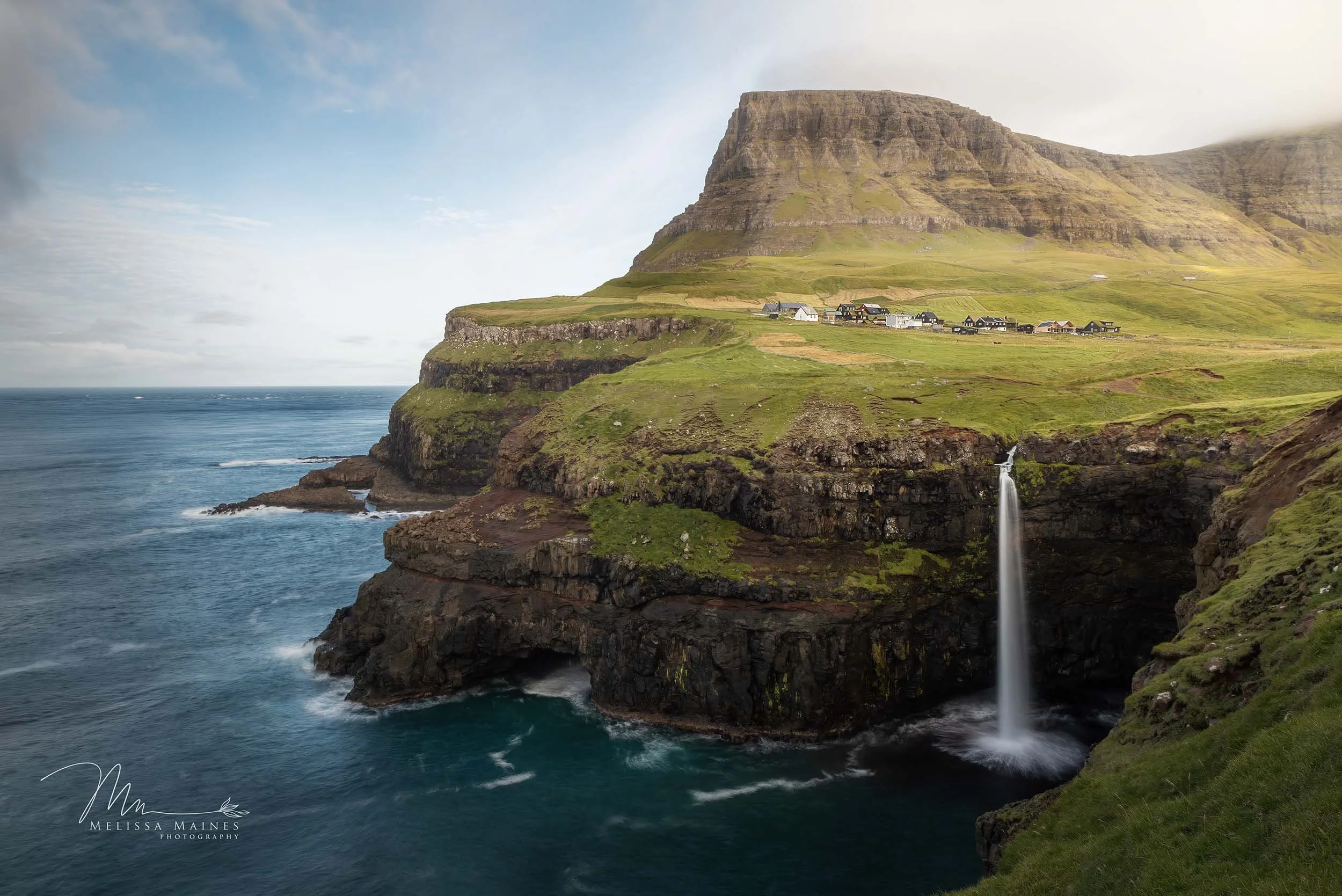 Cliffside Múlafossur Waterfall in the Faroe Islands with the falls streaming directly into the ocean.