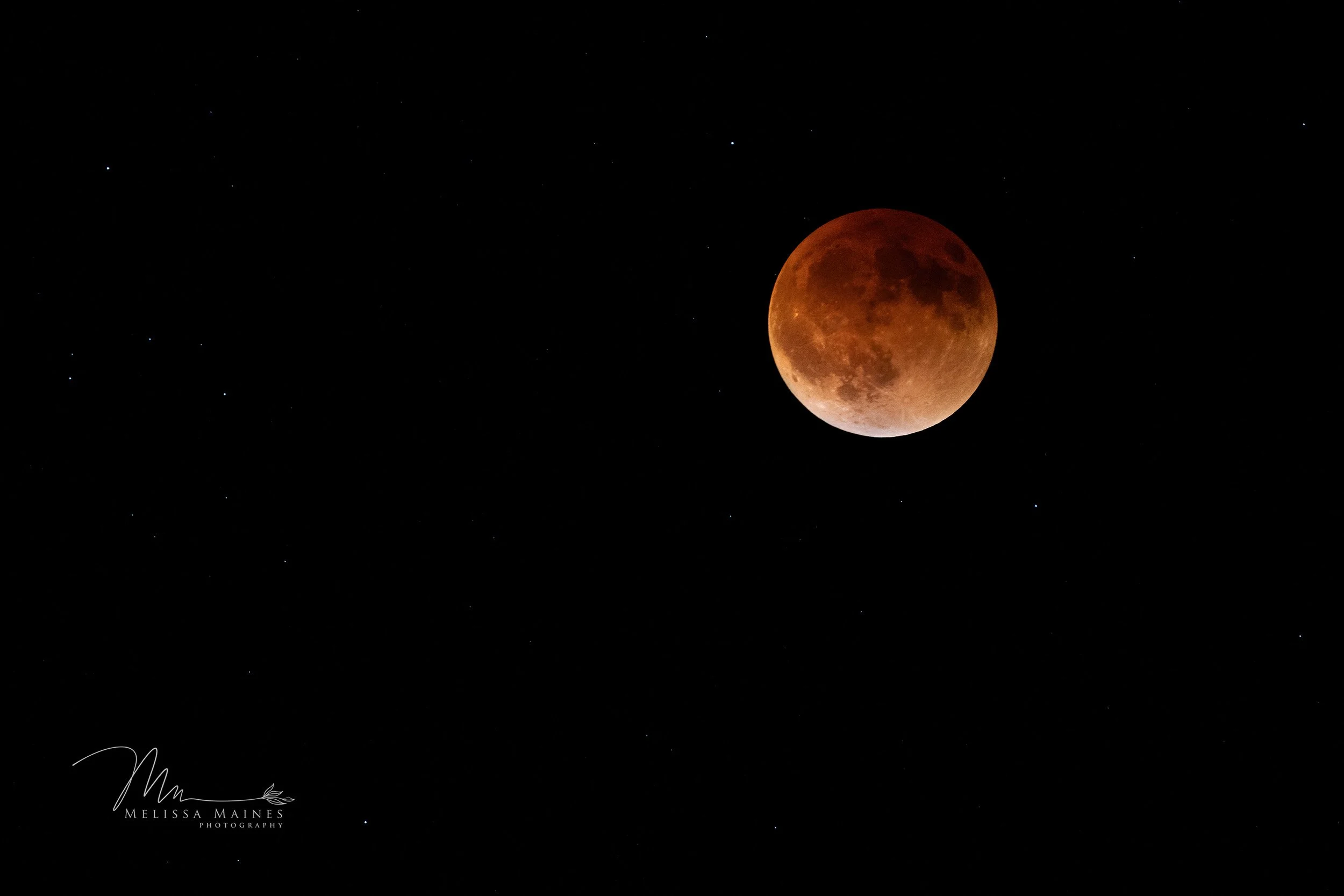 A red-orange lunar eclipse with the moon in a reddish hue, surrounded by stars in the dark night sky.