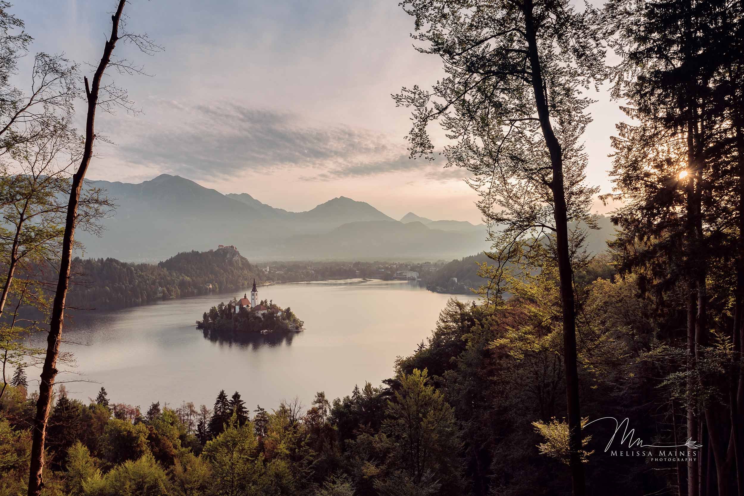 A scenic landscape of a Lake Bled with a small island featuring a church and a tall steeple, in Slovenia