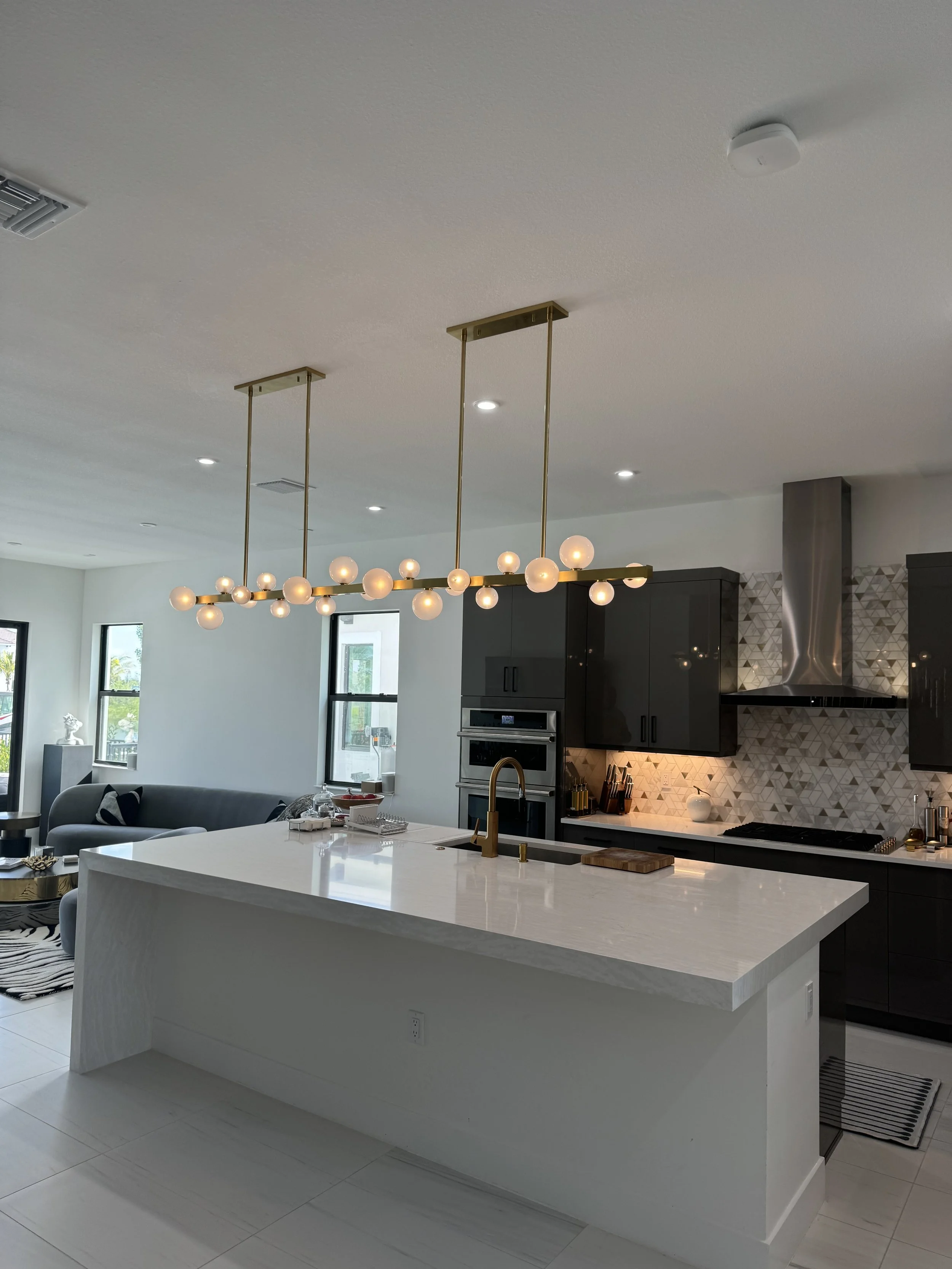 Modern kitchen with white island, black cabinets, geometric backsplash, and gold pendant lighting.