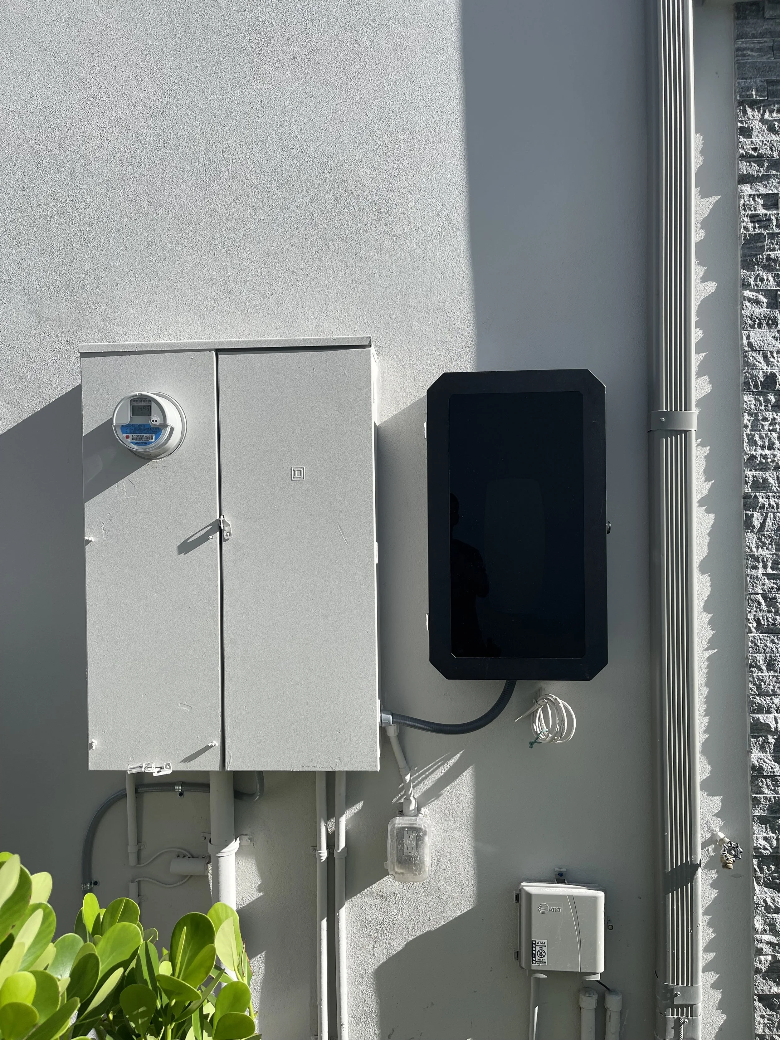 External wall with electrical meters, boxes, wiring, and conduit pipe.