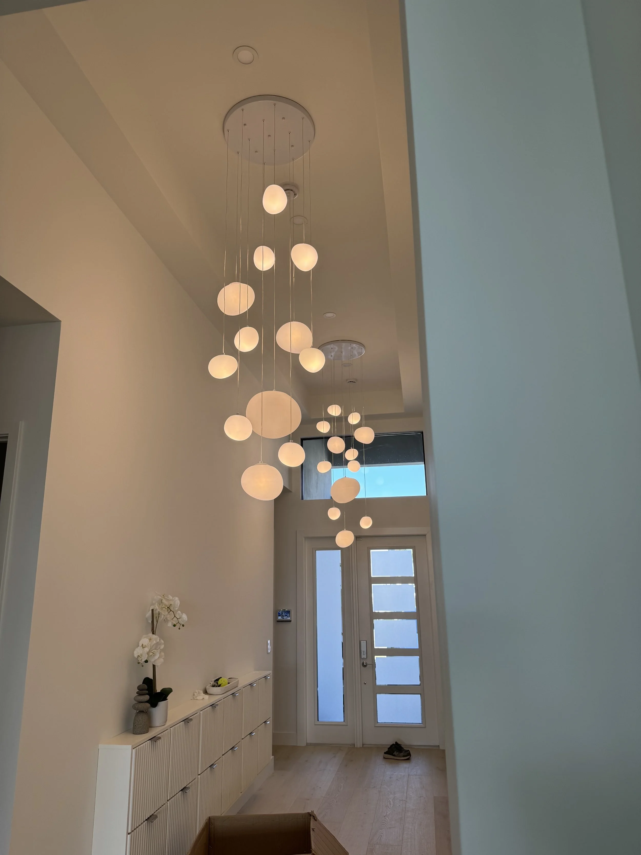 Modern foyer with a cluster of hanging pendant lights with globe-shaped bulbs, a white sideboard, decorative items, and a front door with glass panels.