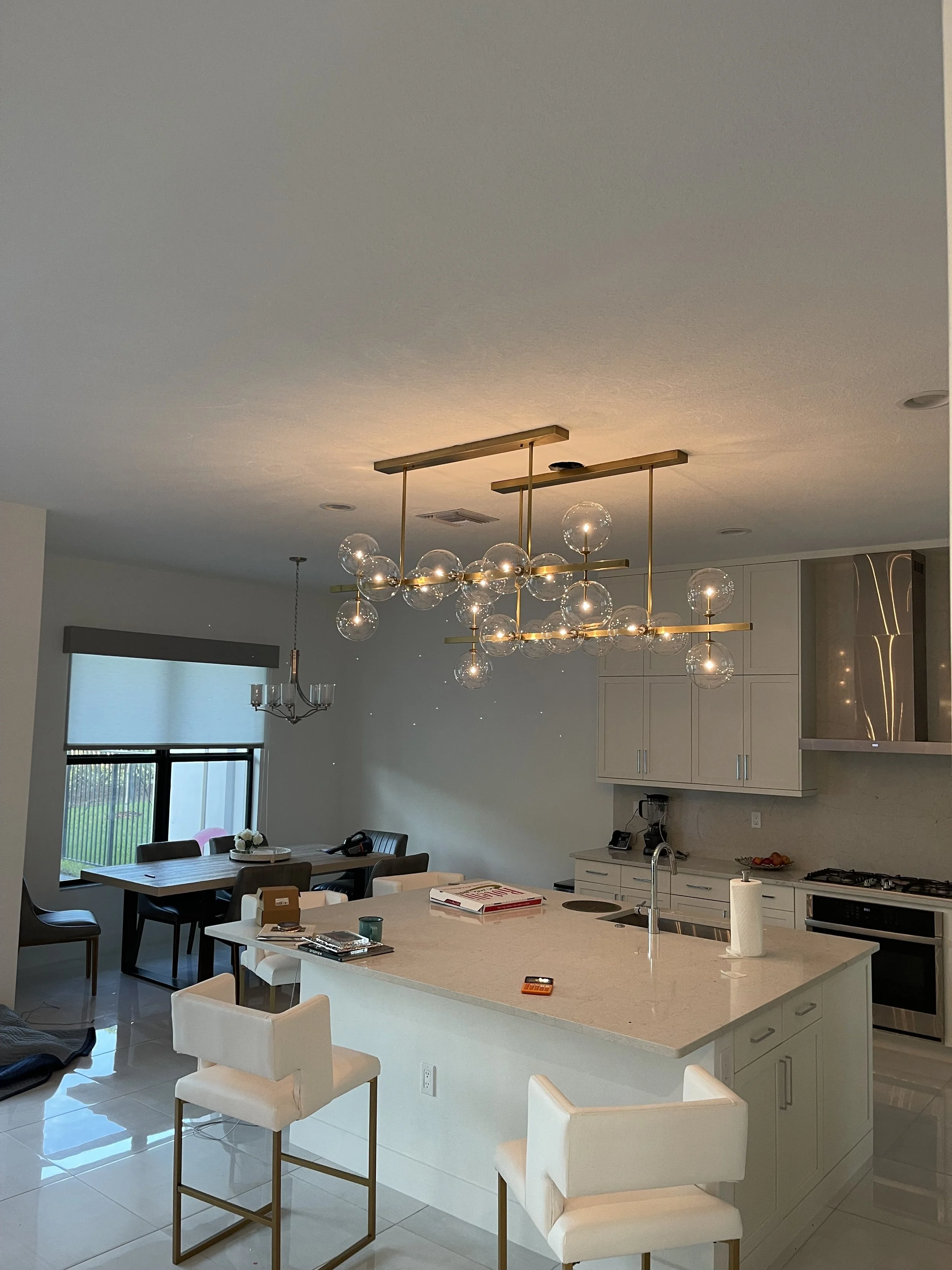 Modern open-concept kitchen with a large island, white cabinets, and contemporary chandelier with glass globes.