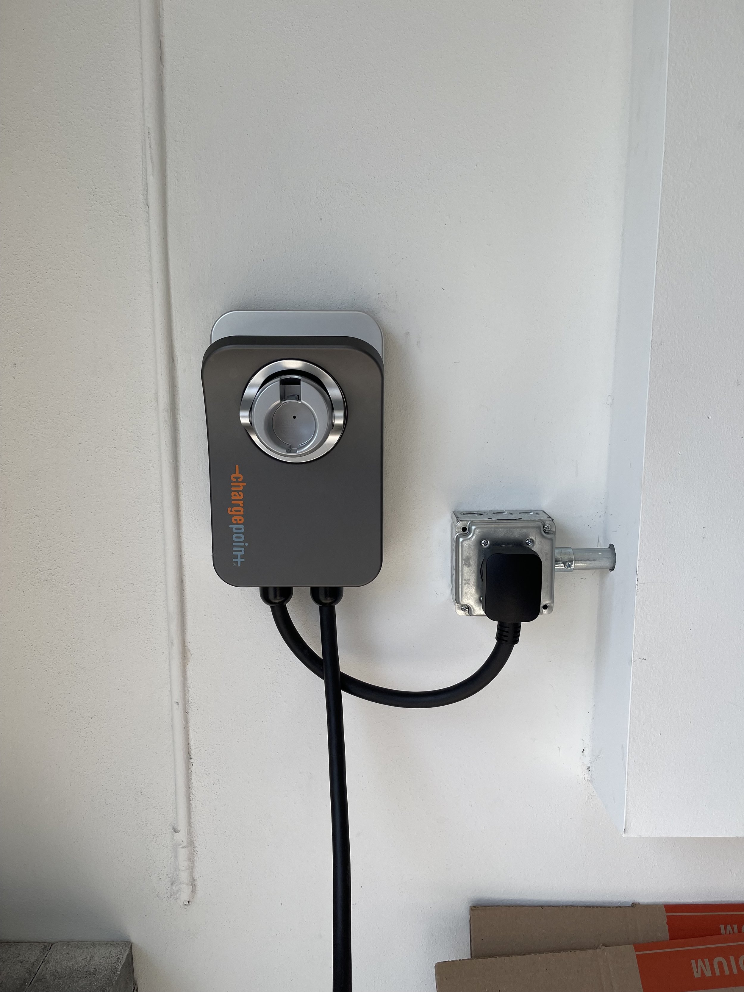 An electric vehicle charging station mounted on a white wall, with a power socket nearby.