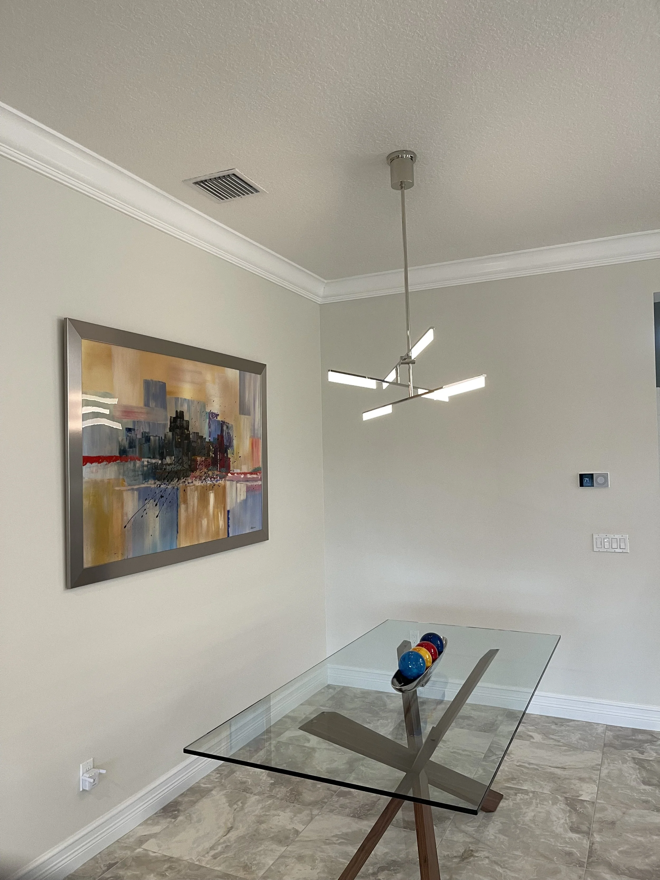 Modern dining room with a glass table, abstract painting, and a contemporary chandelier.
