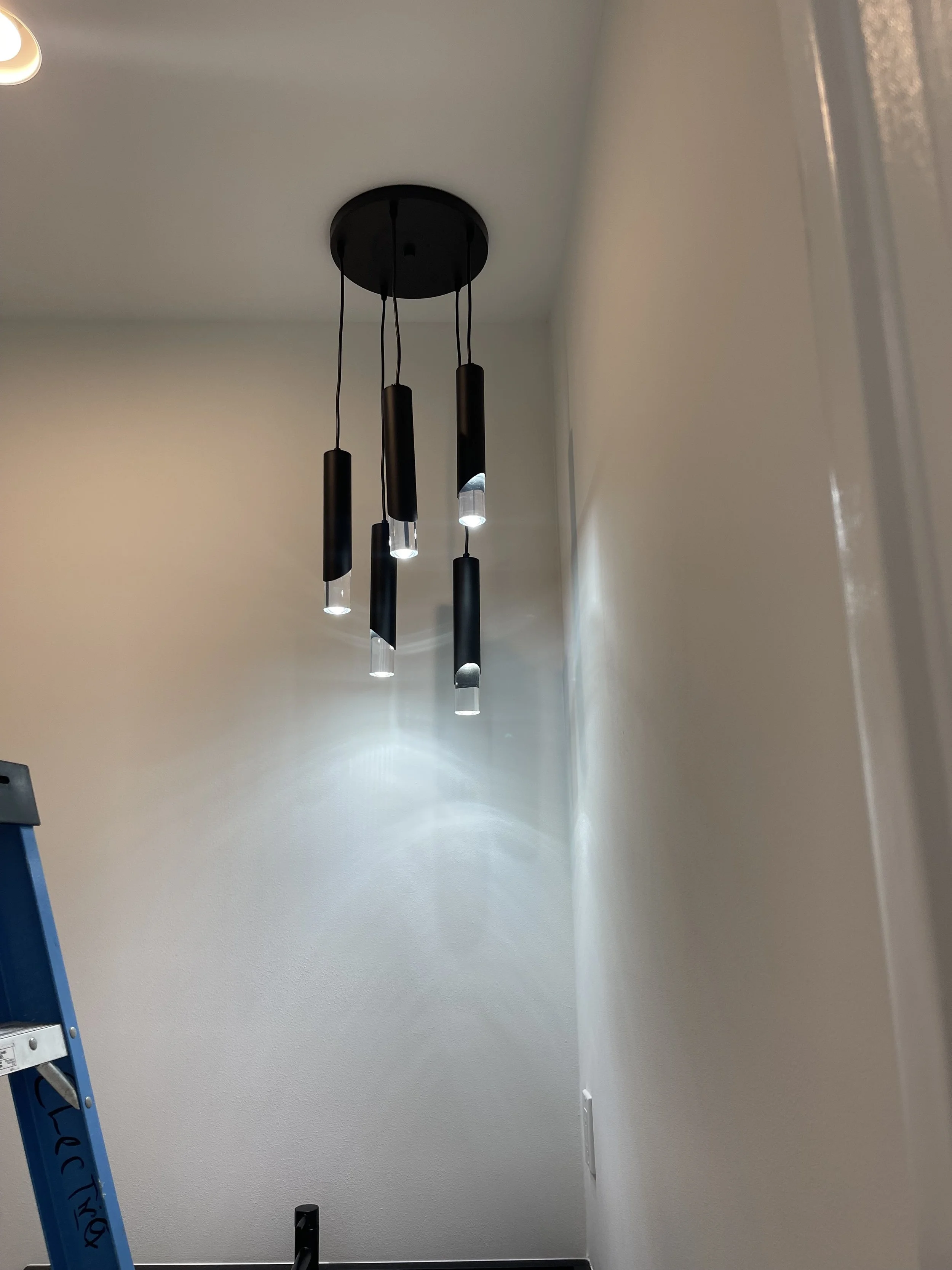 A modern black pendant chandelier with multiple hanging cylindrical lights on a ceiling in a room.