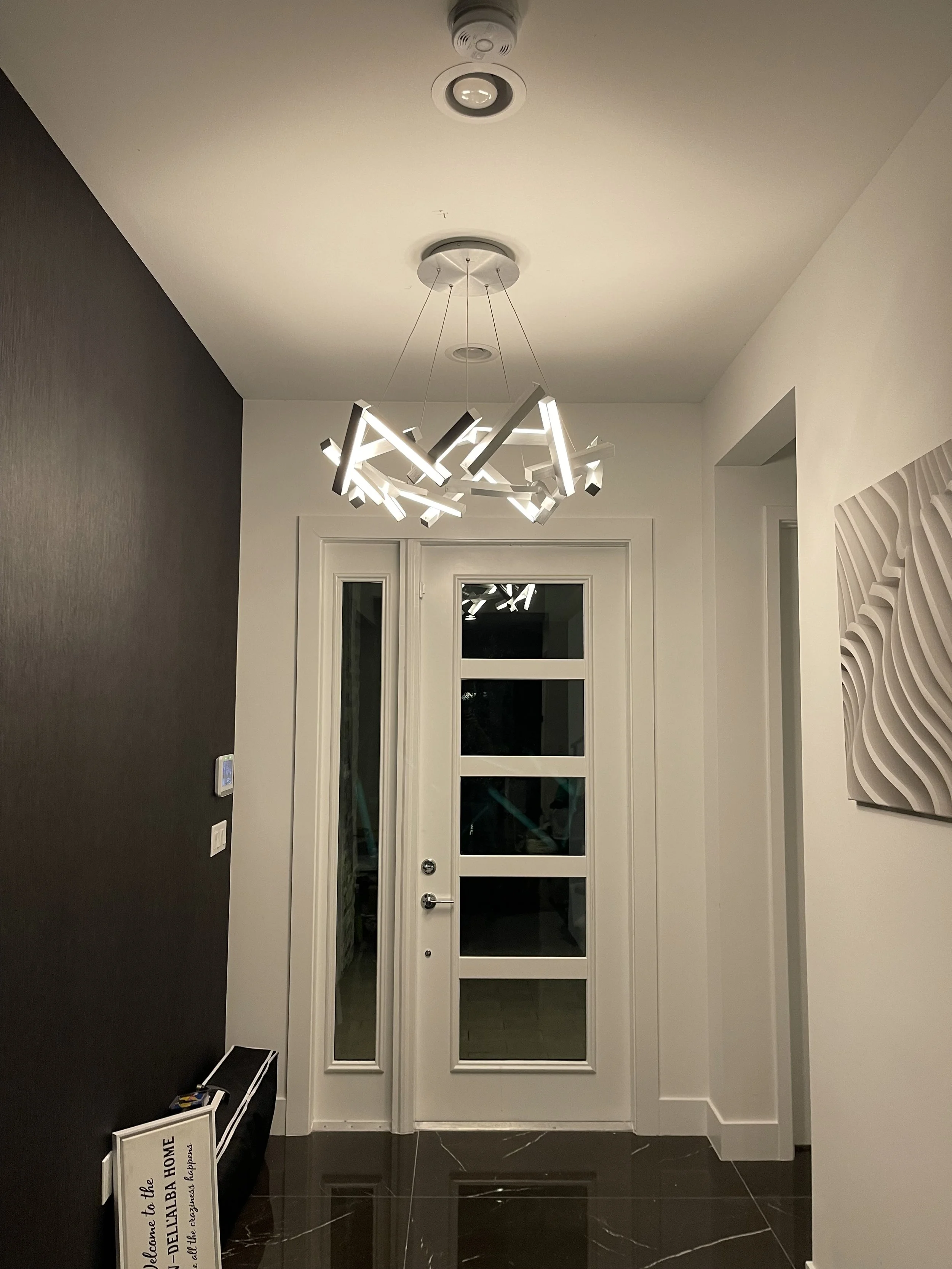 Modern entryway with black tiled floor, white walls, a white door with glass panels, and a contemporary chandelier hanging from the ceiling.