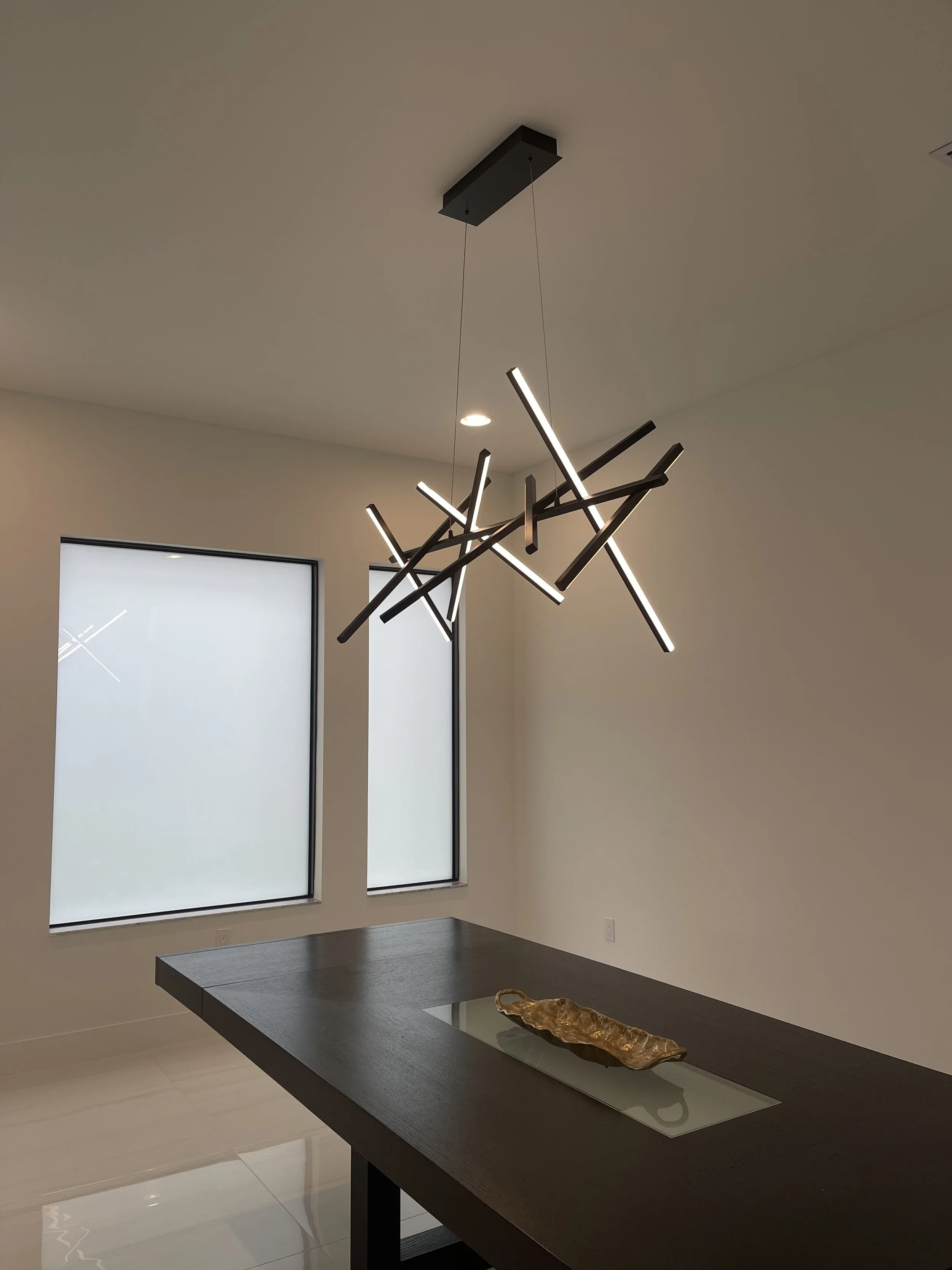 Modern interior dining room with hanging geometric chandelier, black table with decorative piece, and frosted windows.