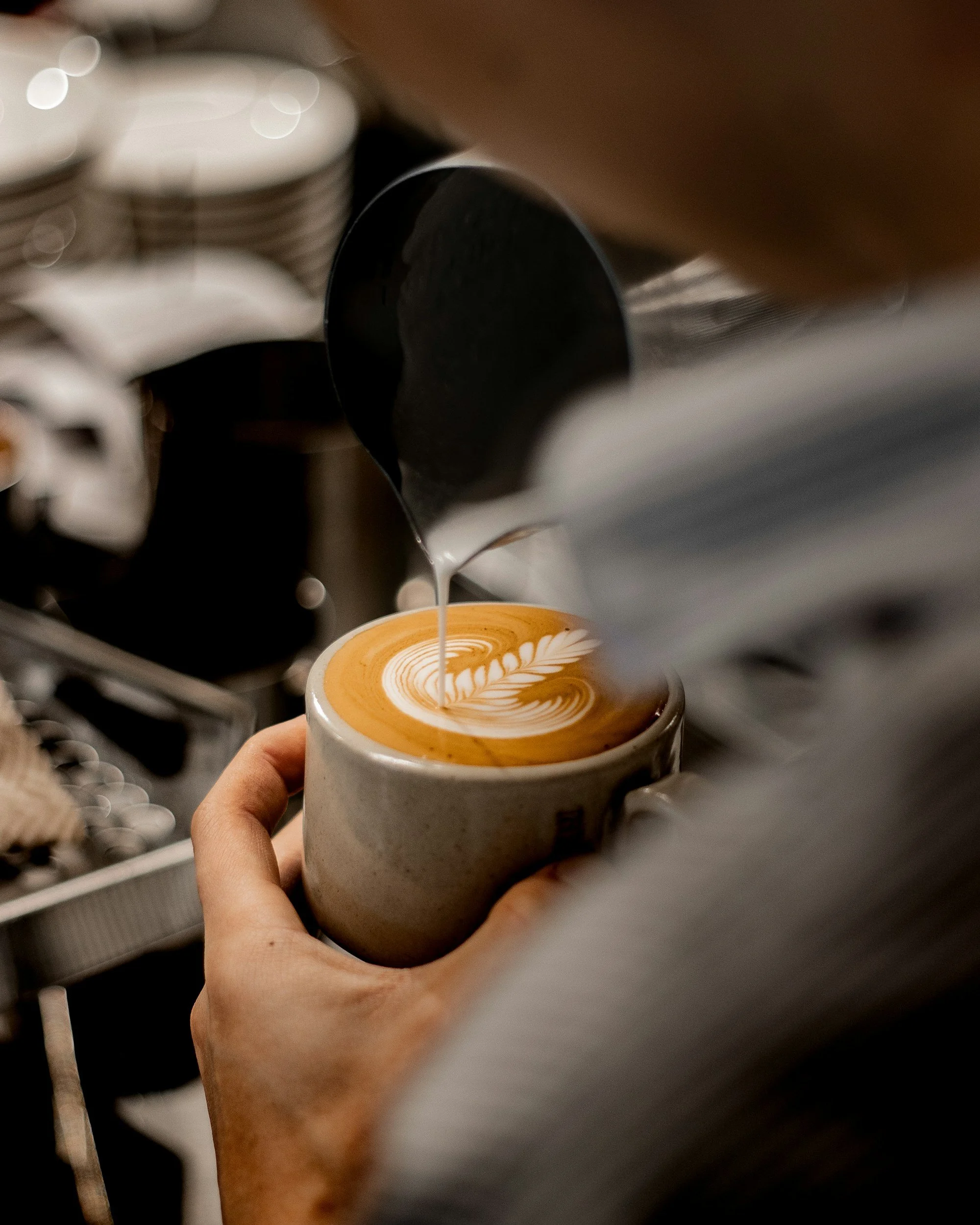 Barista pouring steamed milk into a coffee cup to create latte art.
