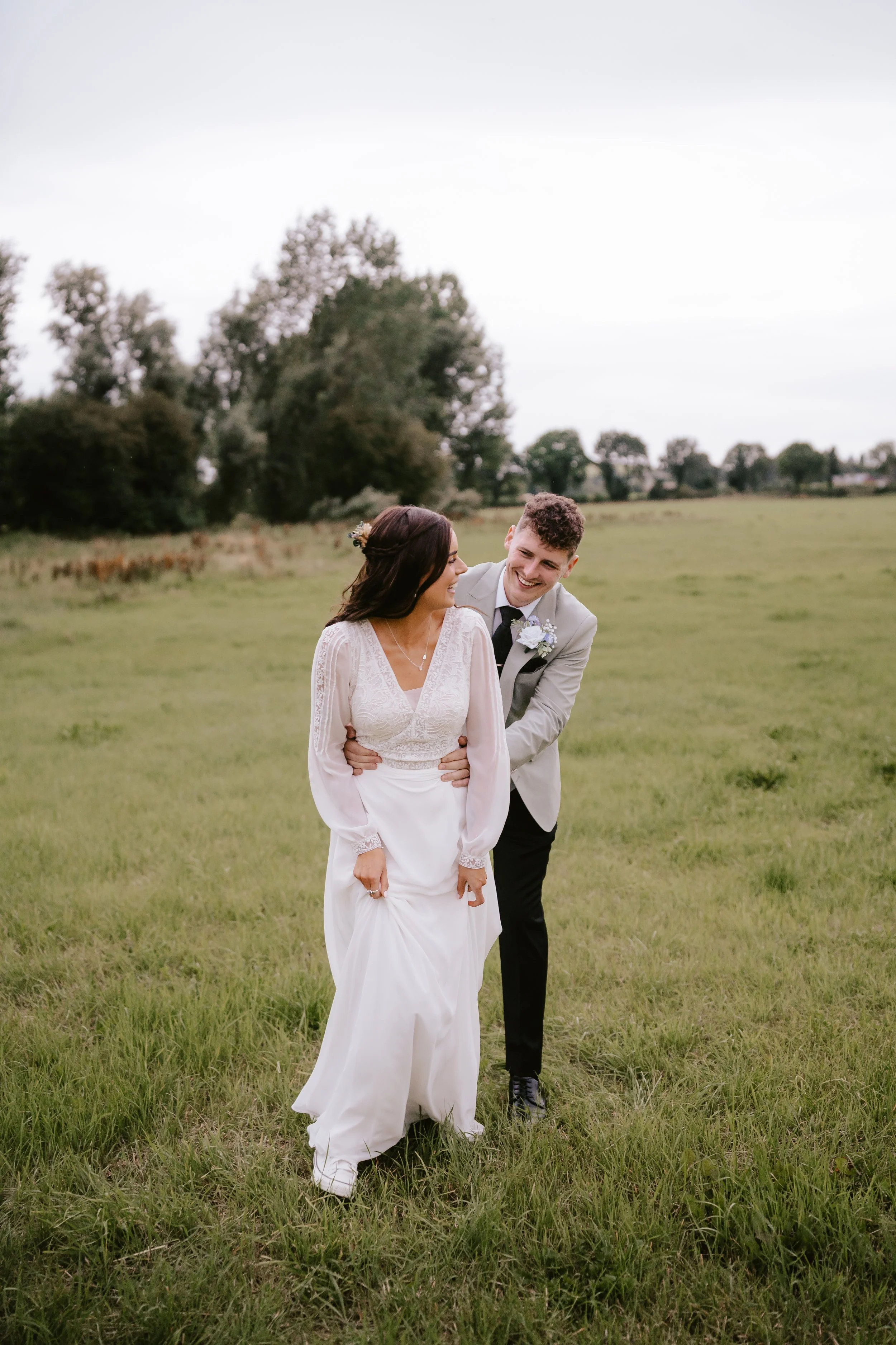 A bride and groom walking in a grassy field, smiling and enjoying each other's company.