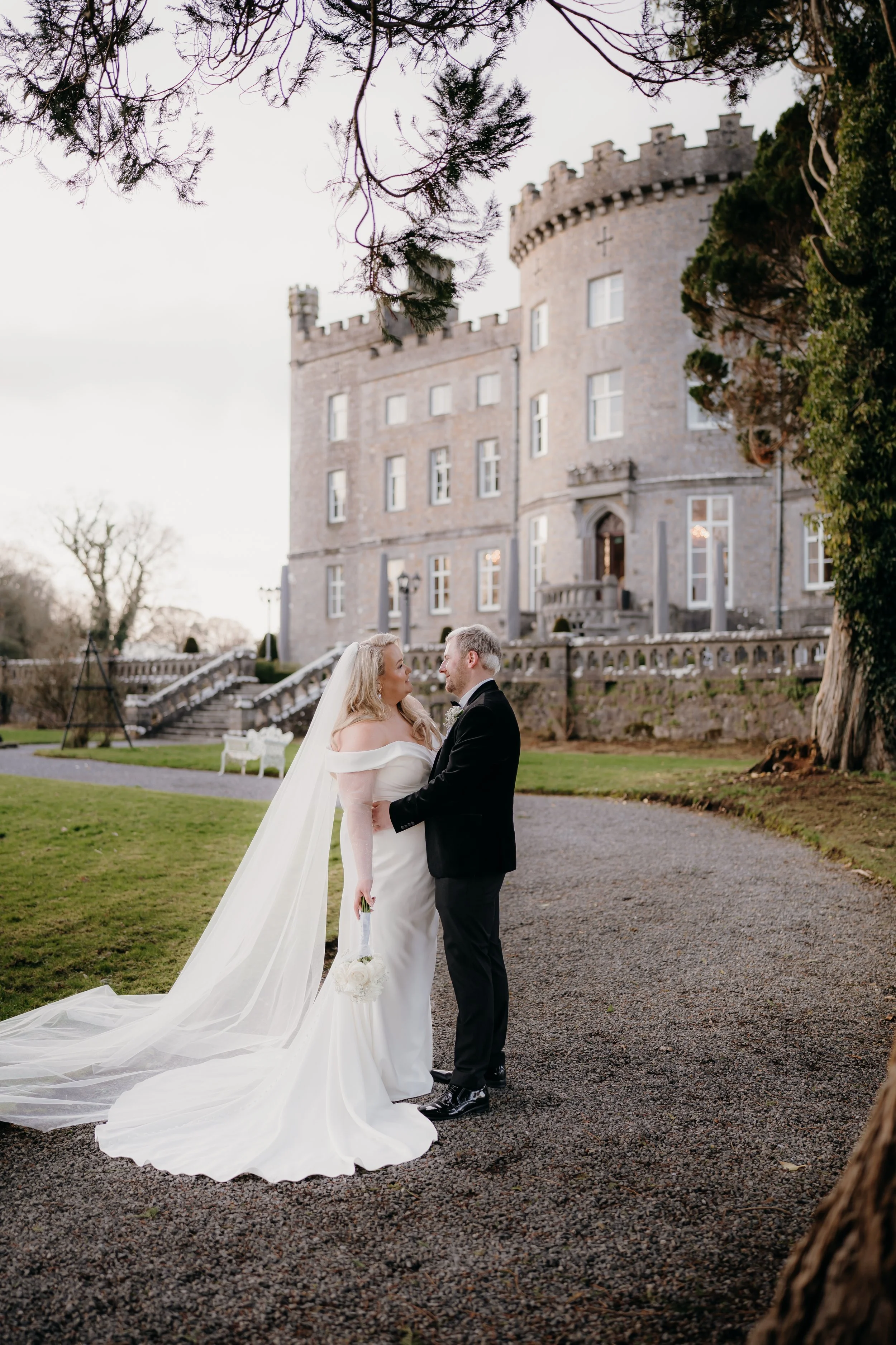Bride and groom standing face to face outside with a castle in the background during their wedding.
