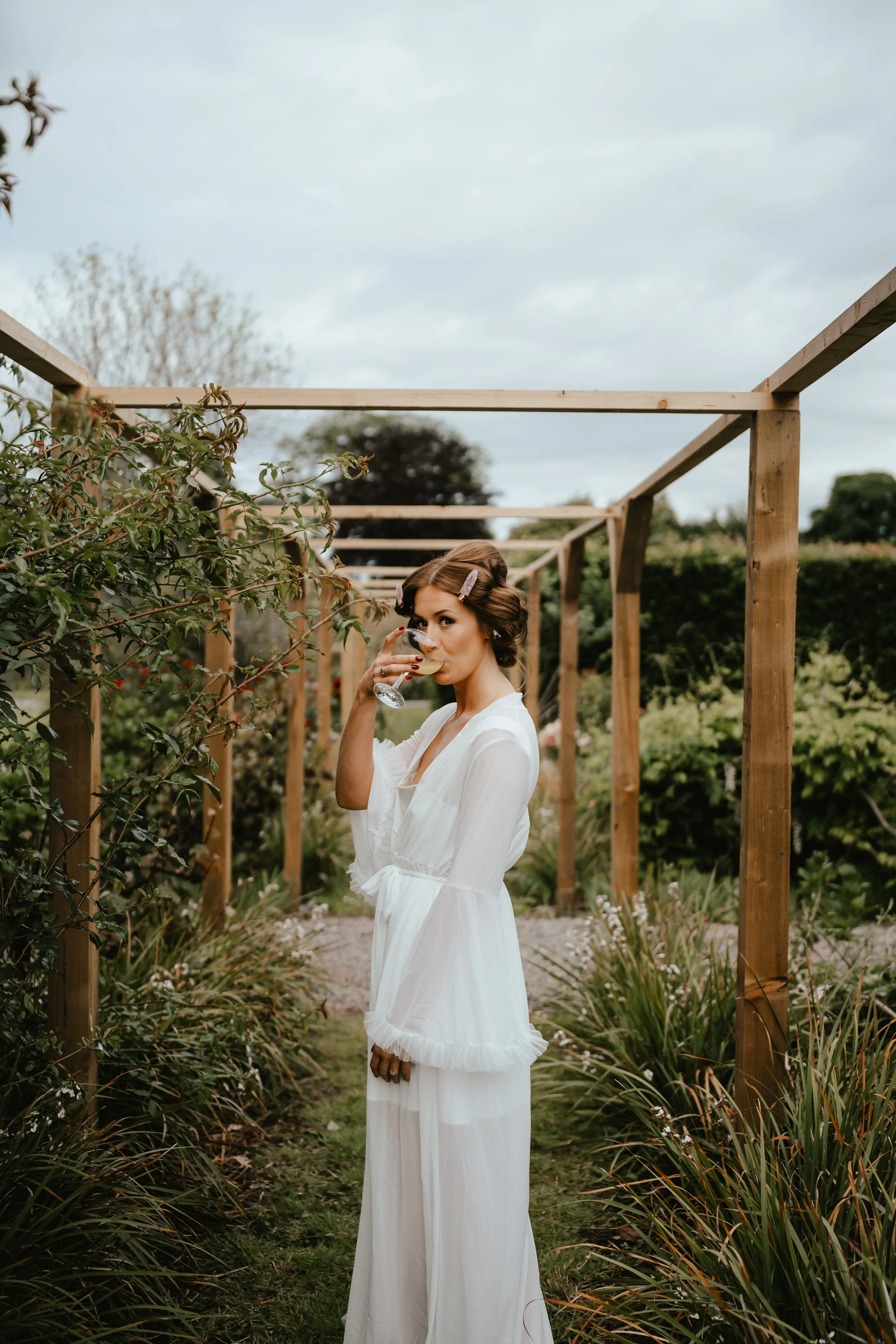 Woman in white dress with curlers in her hair sipping wine in a garden.