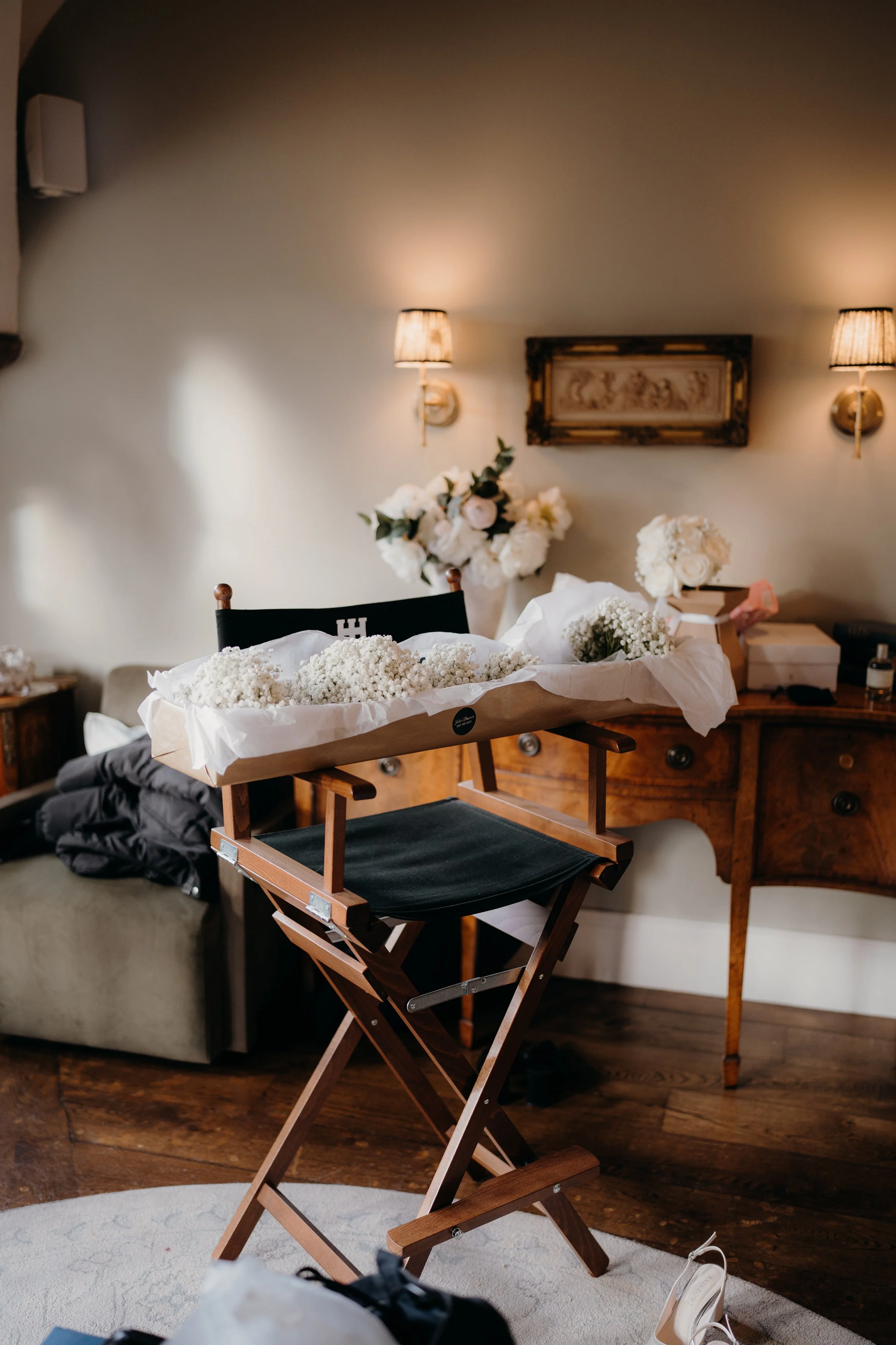 A cozy room with a wooden chair and a table, decorated with white flowers, and two wall lamps with beige shades.