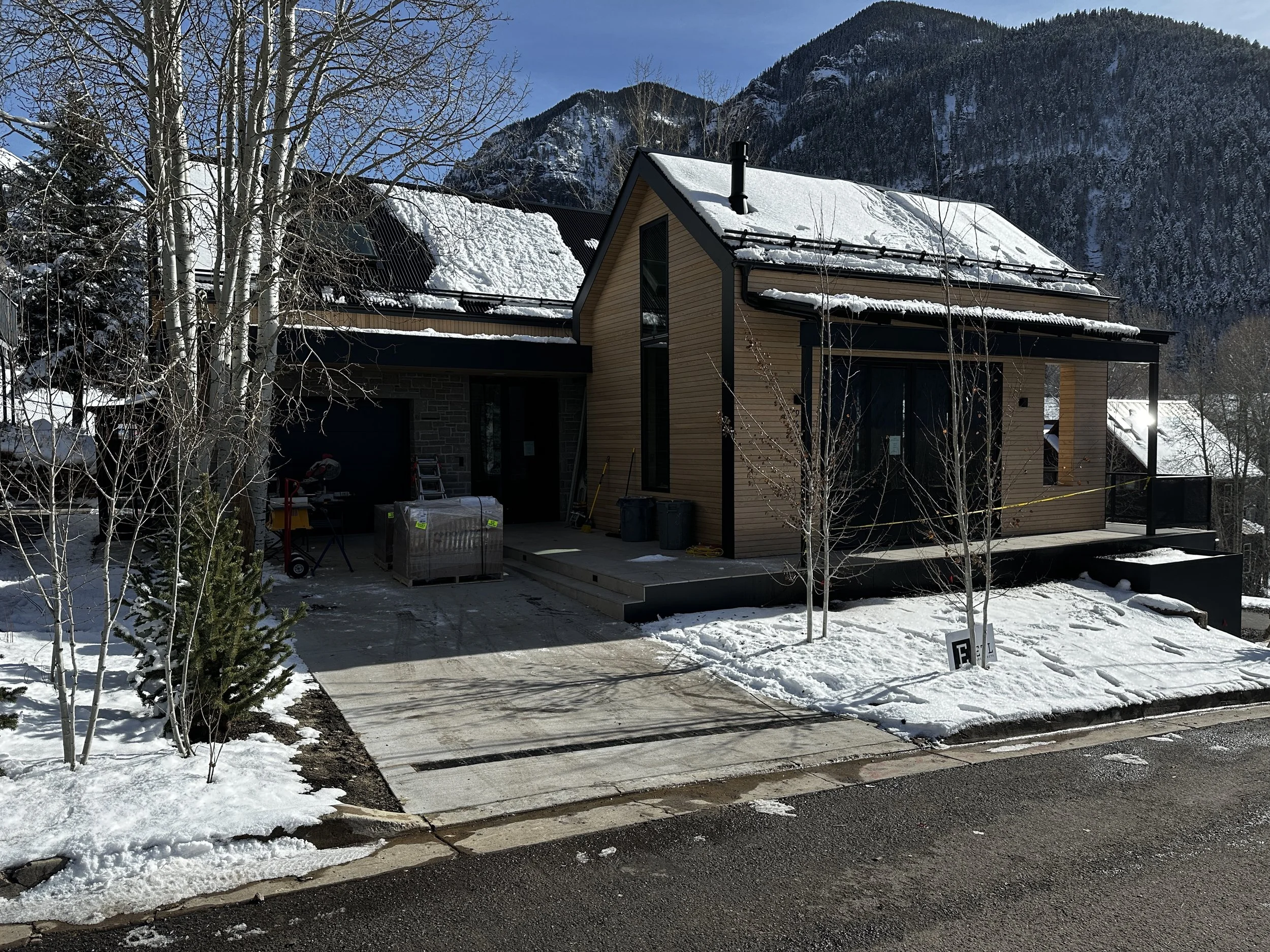 Newly built house in a snowy mountain landscape with construction materials in the driveway.