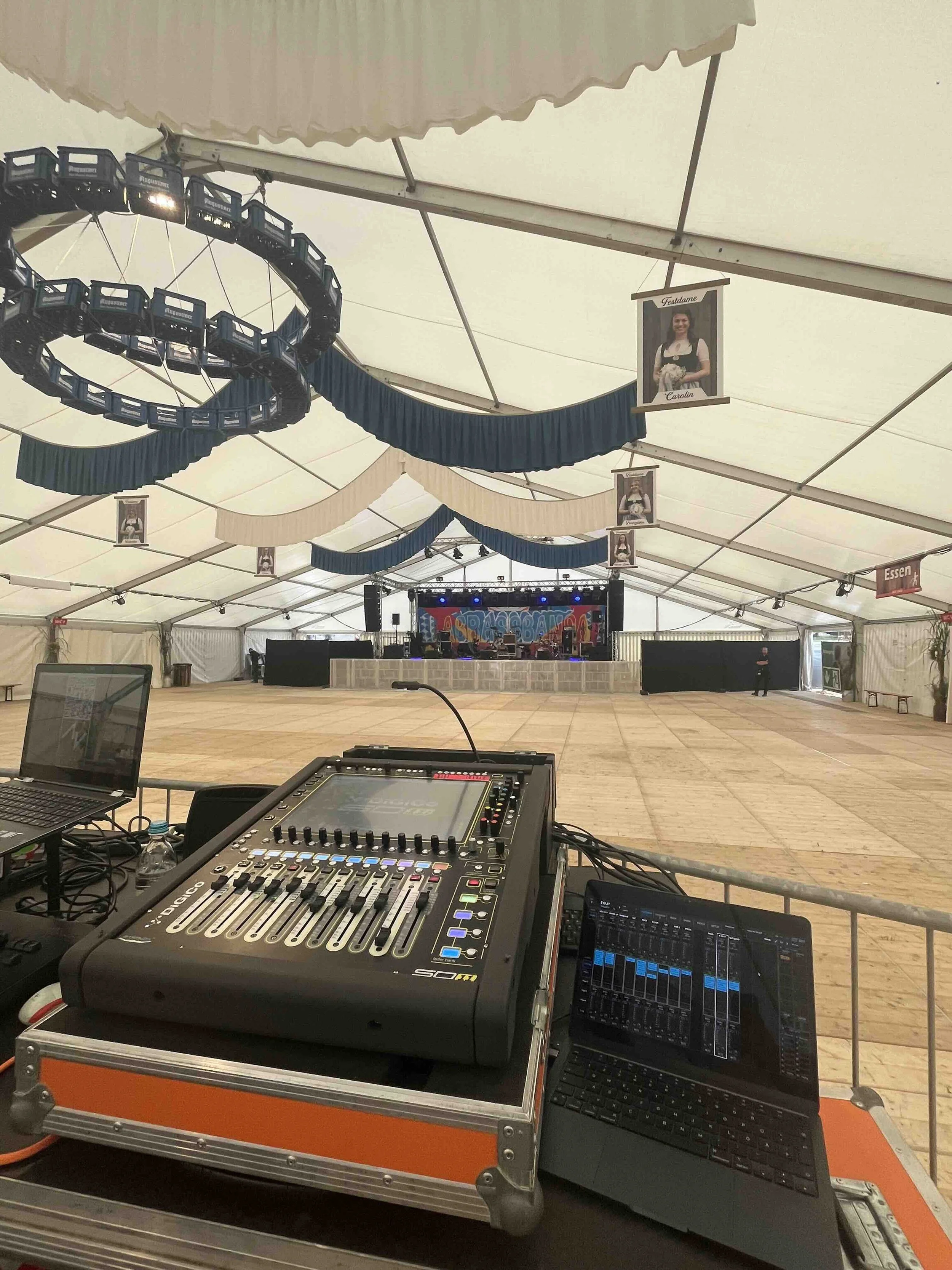 Innenaufnahme eines großen Festzelts mit einem Digico Tonmischpult im Vordergrund. Im Hintergrund ist eine große Bühne mit dem Schriftzug der Band LaBrassBanda.