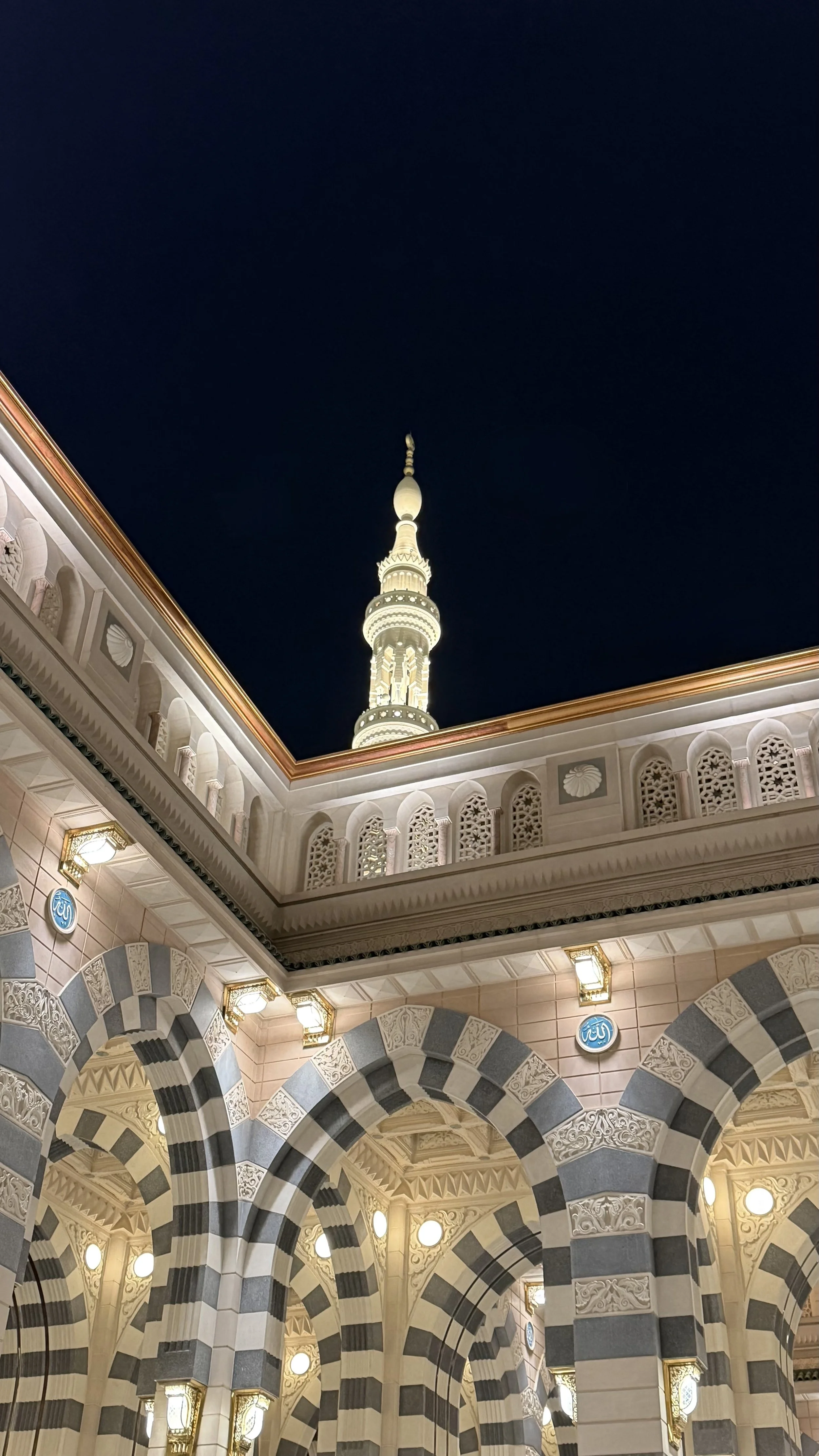 Vue nocturne d'une mosquée avec un minaret illuminé, arches ornées, et décorations arabesques.