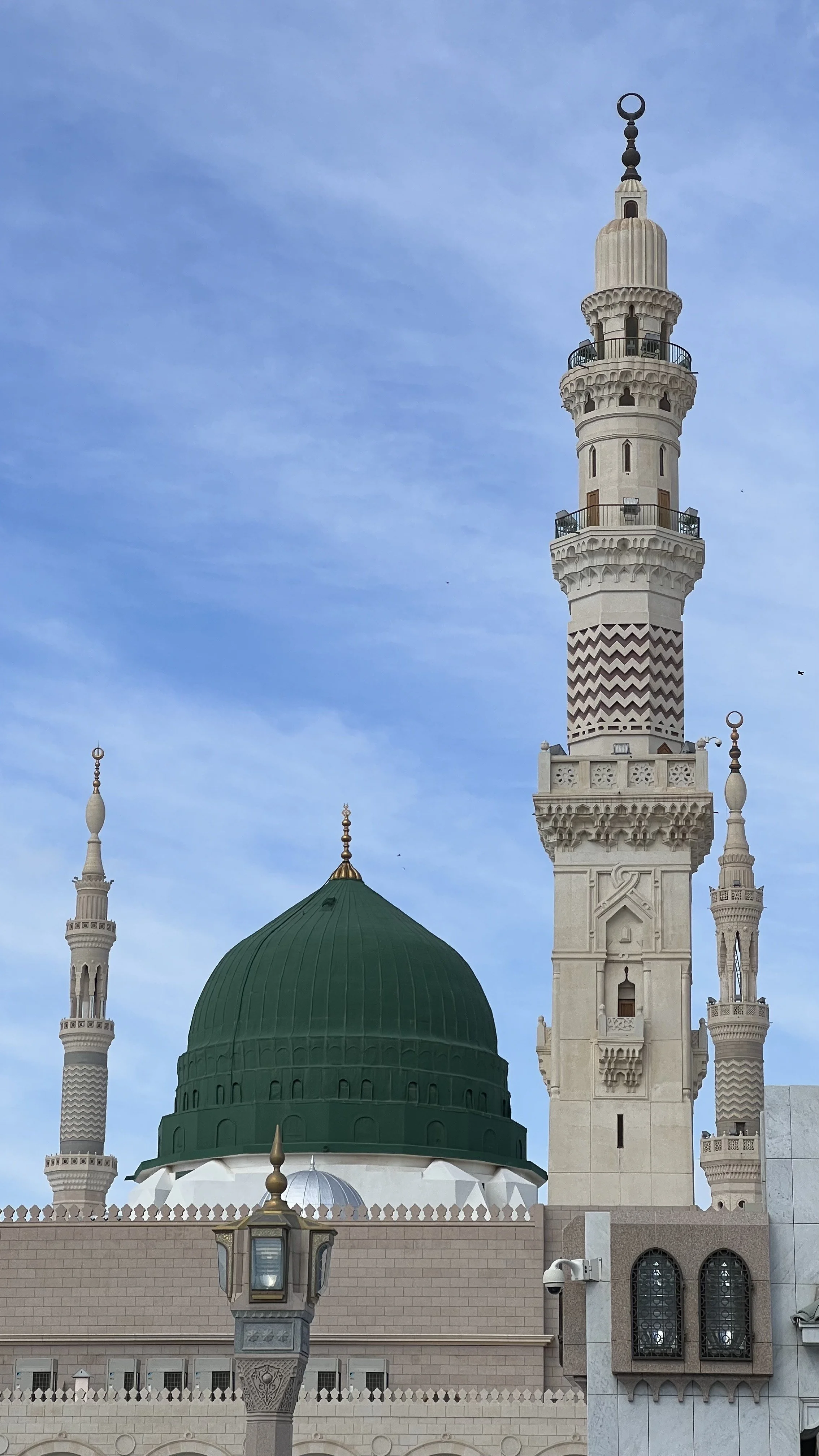 Une mosquée avec un dôme vert et une minaret blanche contre un ciel bleu.