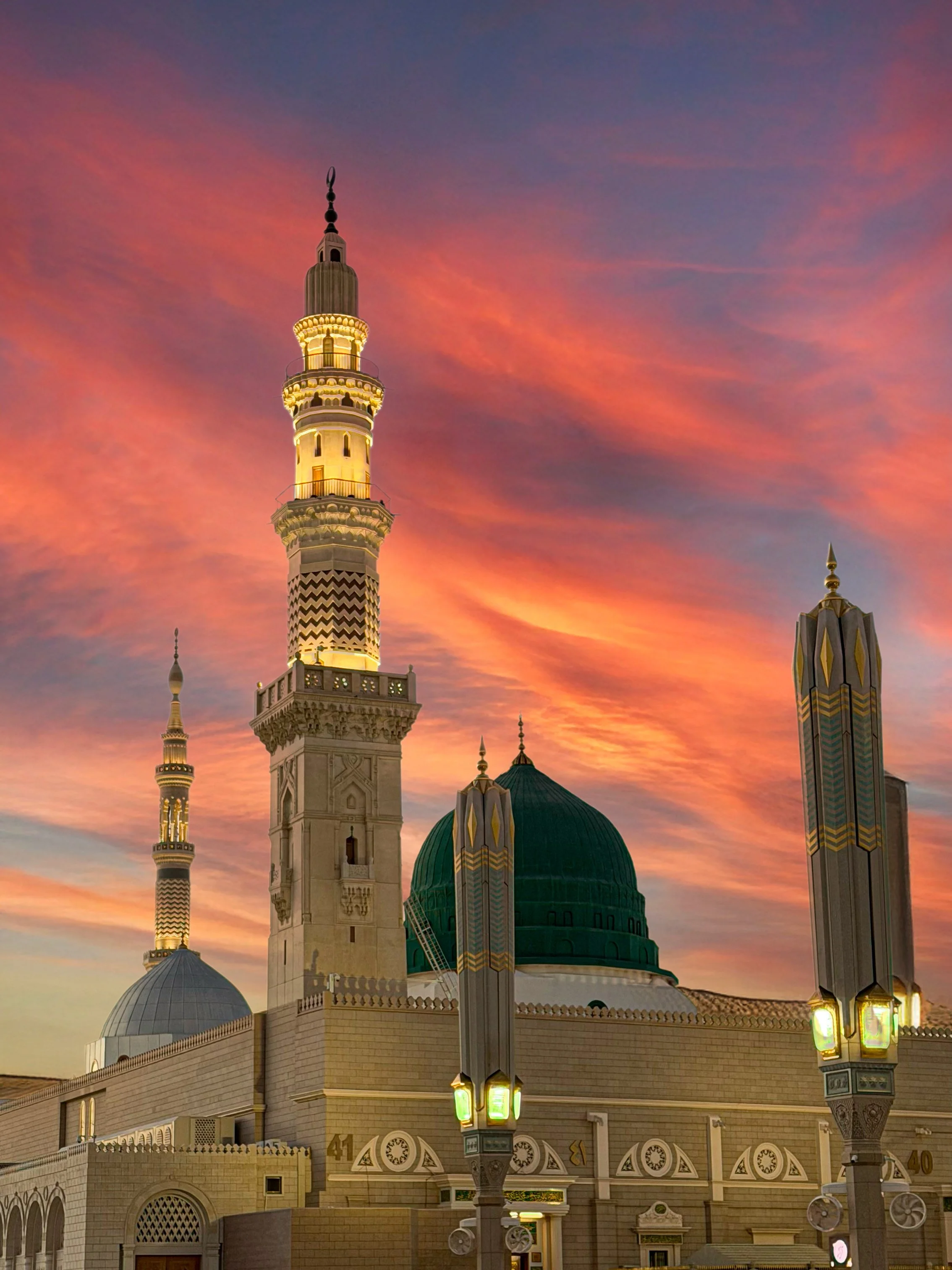 Une mosquée avec un ciel coloré au coucher du soleil, grande minarets illuminés, architecture islamique, lampadaires devant.