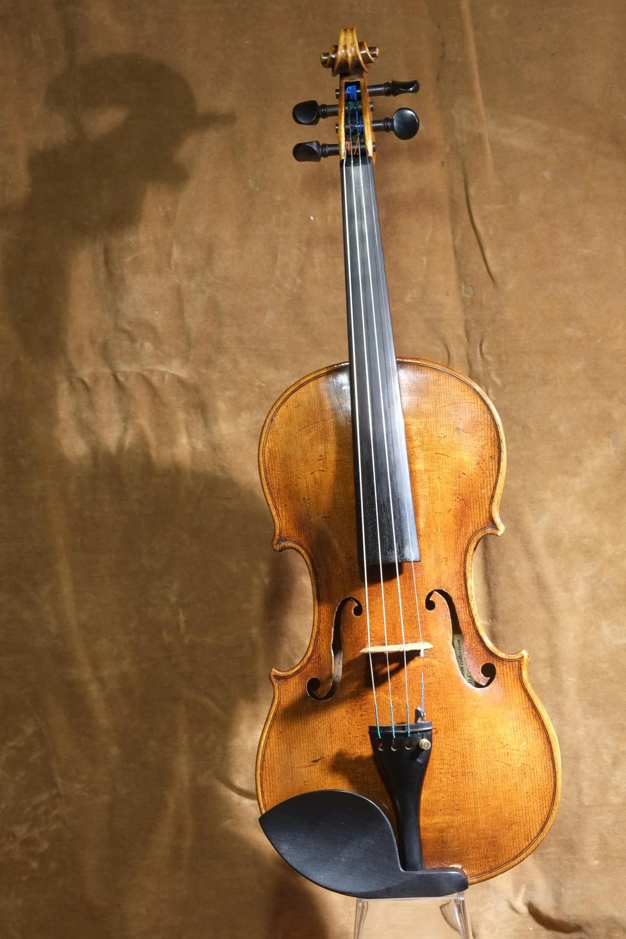 A wooden violin with black tuning pegs and a black chin rest, resting on a clear stand against a brown background.