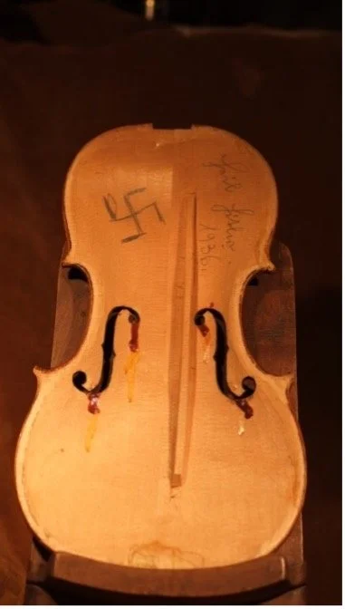 A wooden violin mold with a swastika symbol and handwritten notes. The mold appears unfinished or homemade.