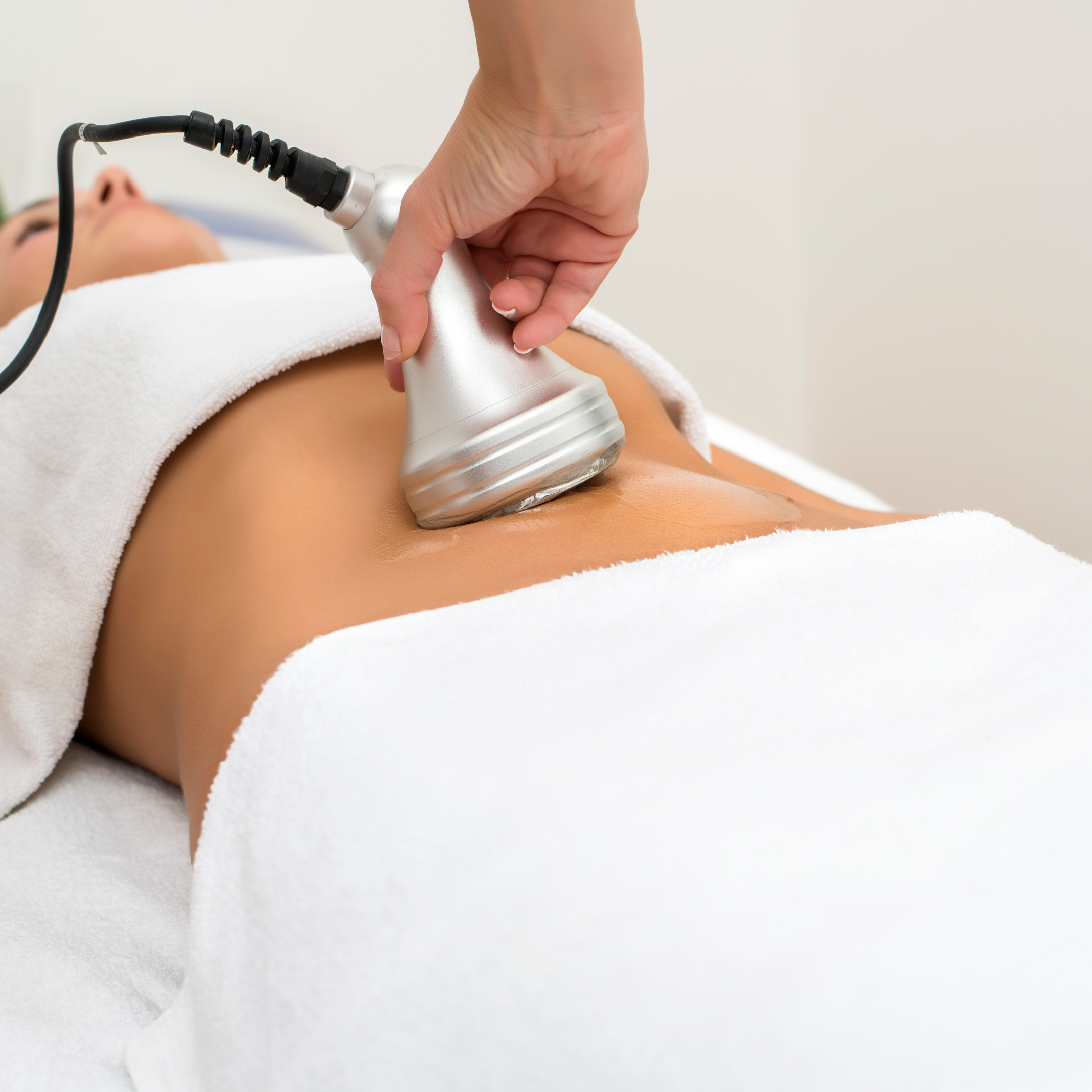A person receiving a cellulite reduction treatment with a handheld device on their abdomen, lying on a spa bed with white towels.