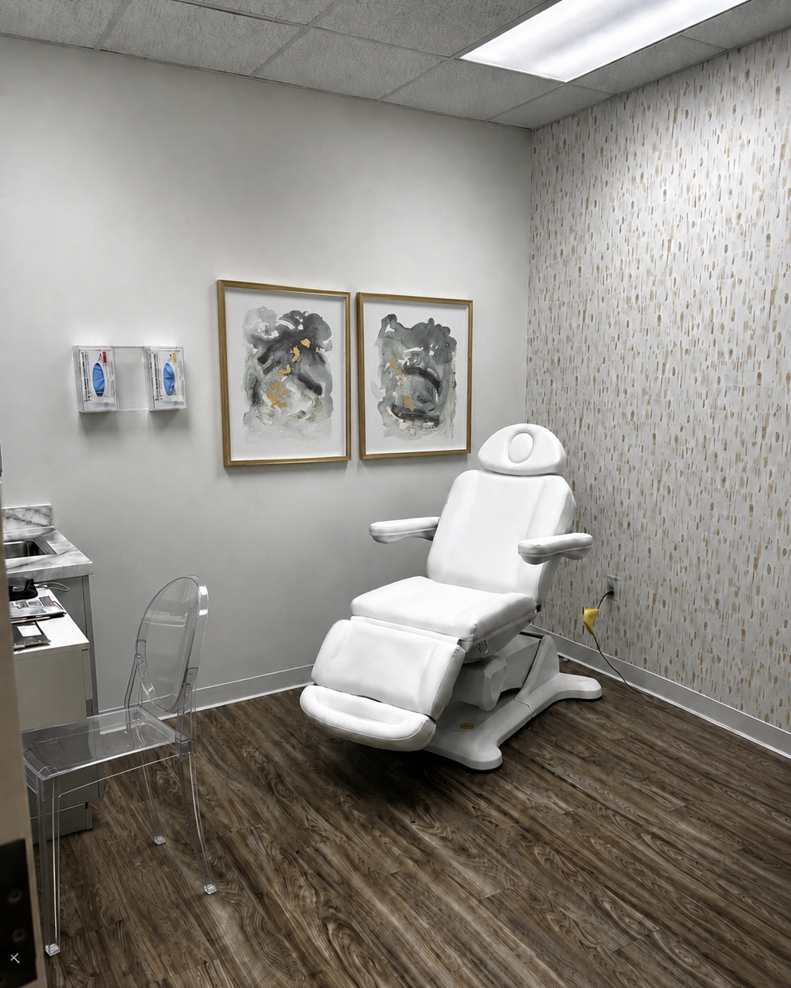 Medical examination room with white leaning chair, abstract artwork on the wall, soap dispensers, and a clear acrylic chair.