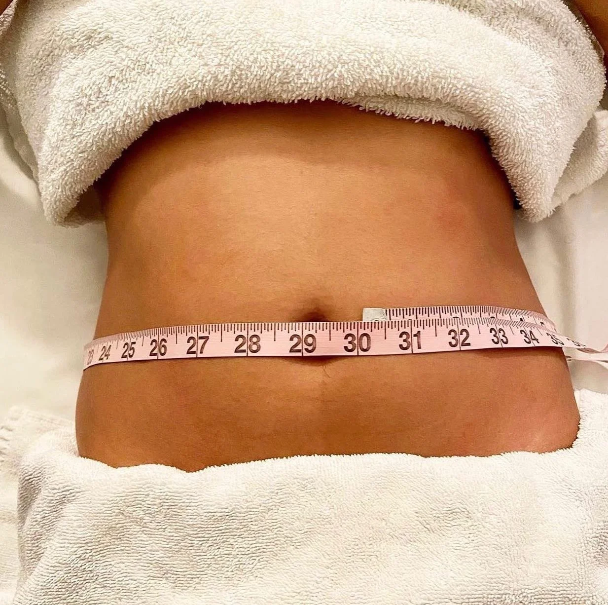 Close-up of a person's waist with a pink measuring tape around it, showing approximately 30 inches.