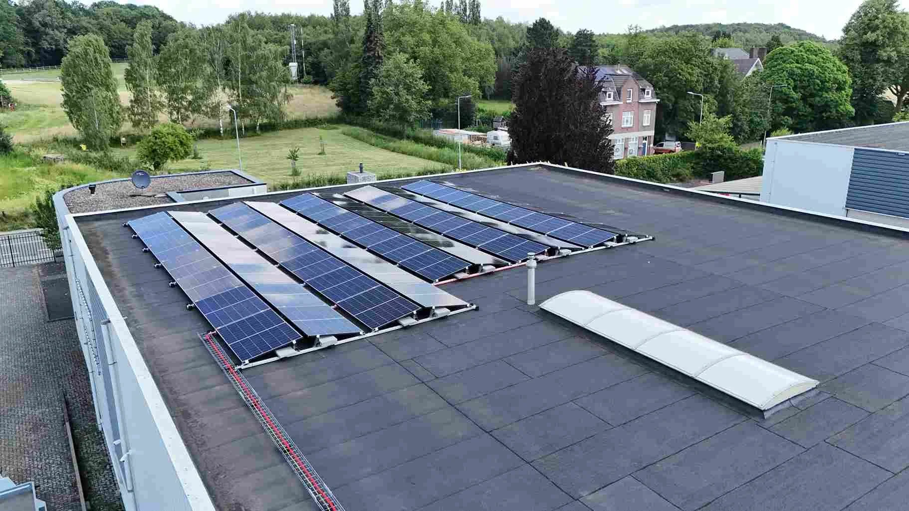 Zonnepanelen op plat dak met groen landschap op de achtergrond.