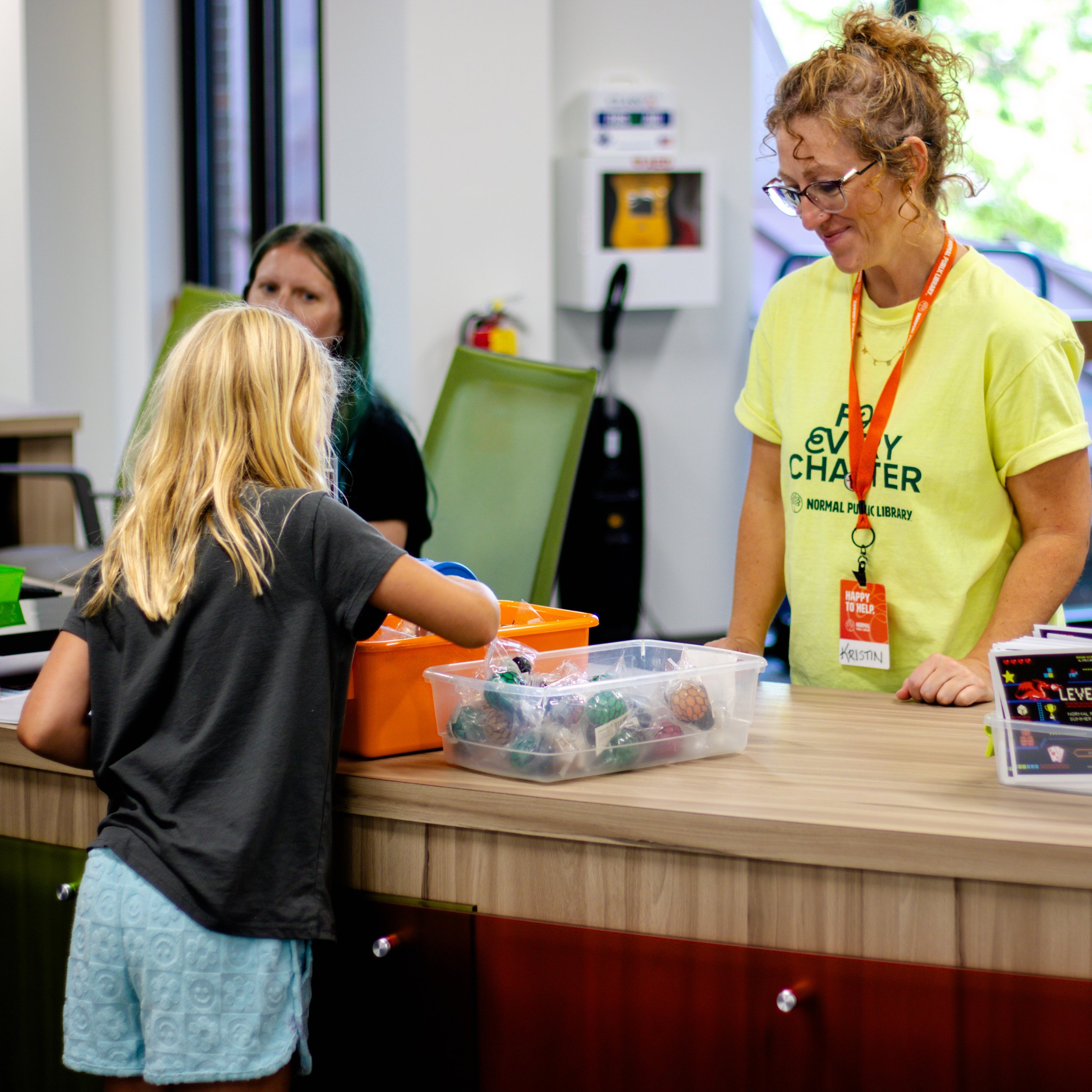 Child looking through a tub of prizes while library employee watches