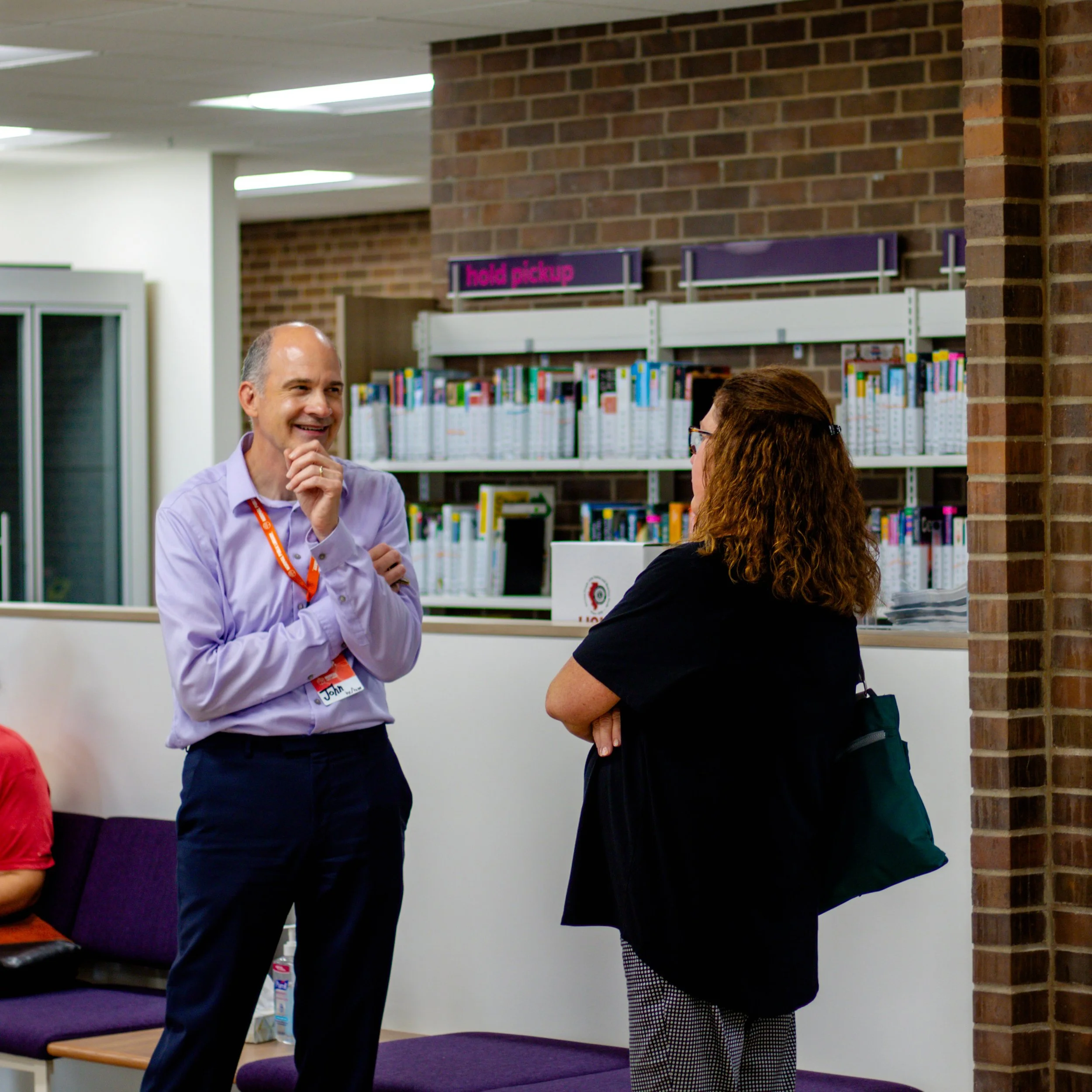Library employee chatting with a patron in front of a book shelf