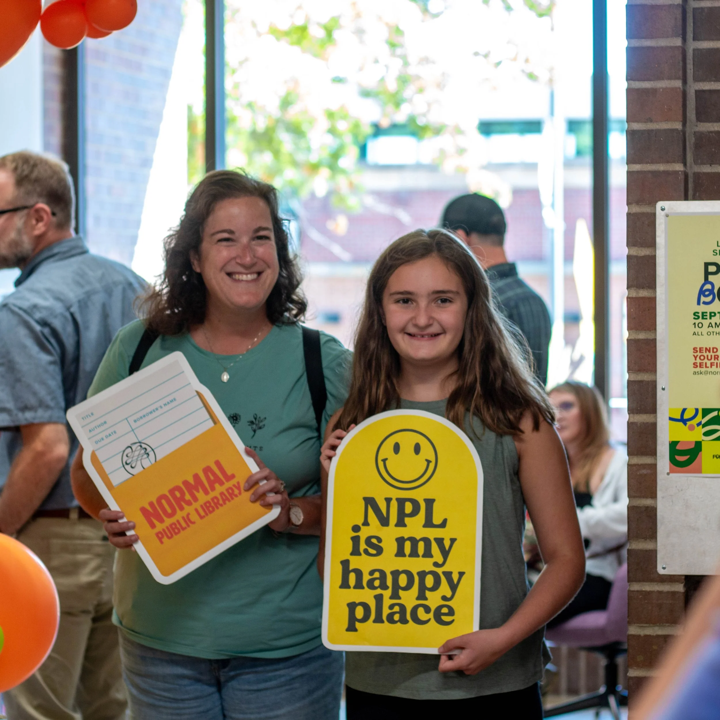Two library patrons smiling and holding library themed signs