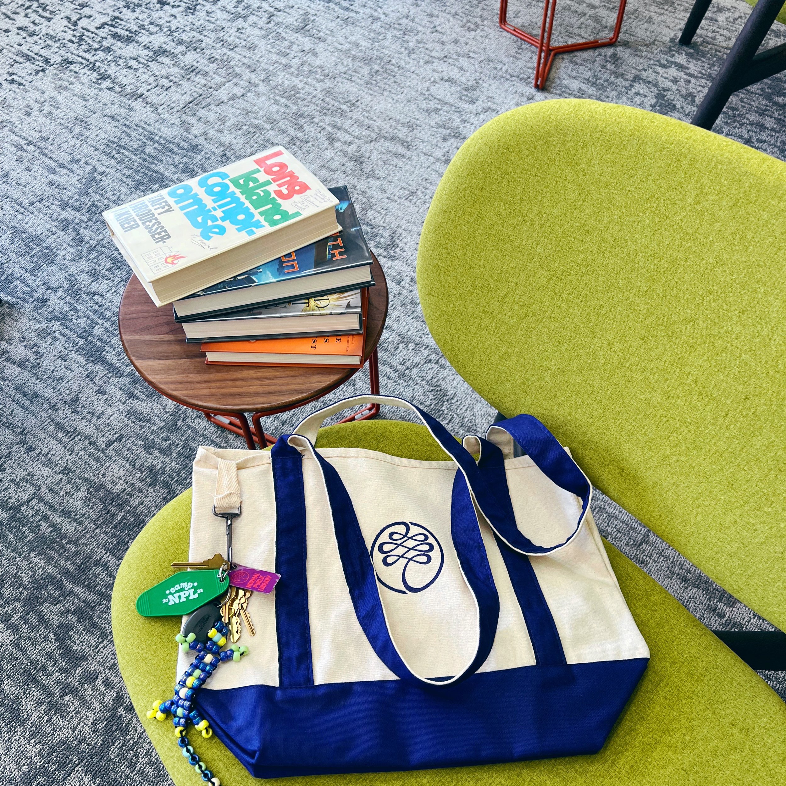 Blue and tan canvas bag with NPL's logo sitting on a bright green chair next to a table with a stack of library books