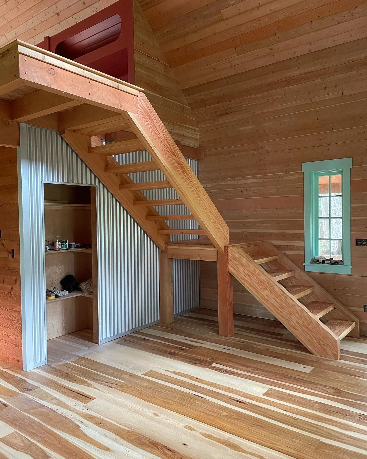 This space features a clean, custom-built interior with a warm, natural wood finish throughout. The focal point is a handcrafted staircase leading to a loft, constructed with solid timber and a modern open-riser design that keeps the space feeling li
