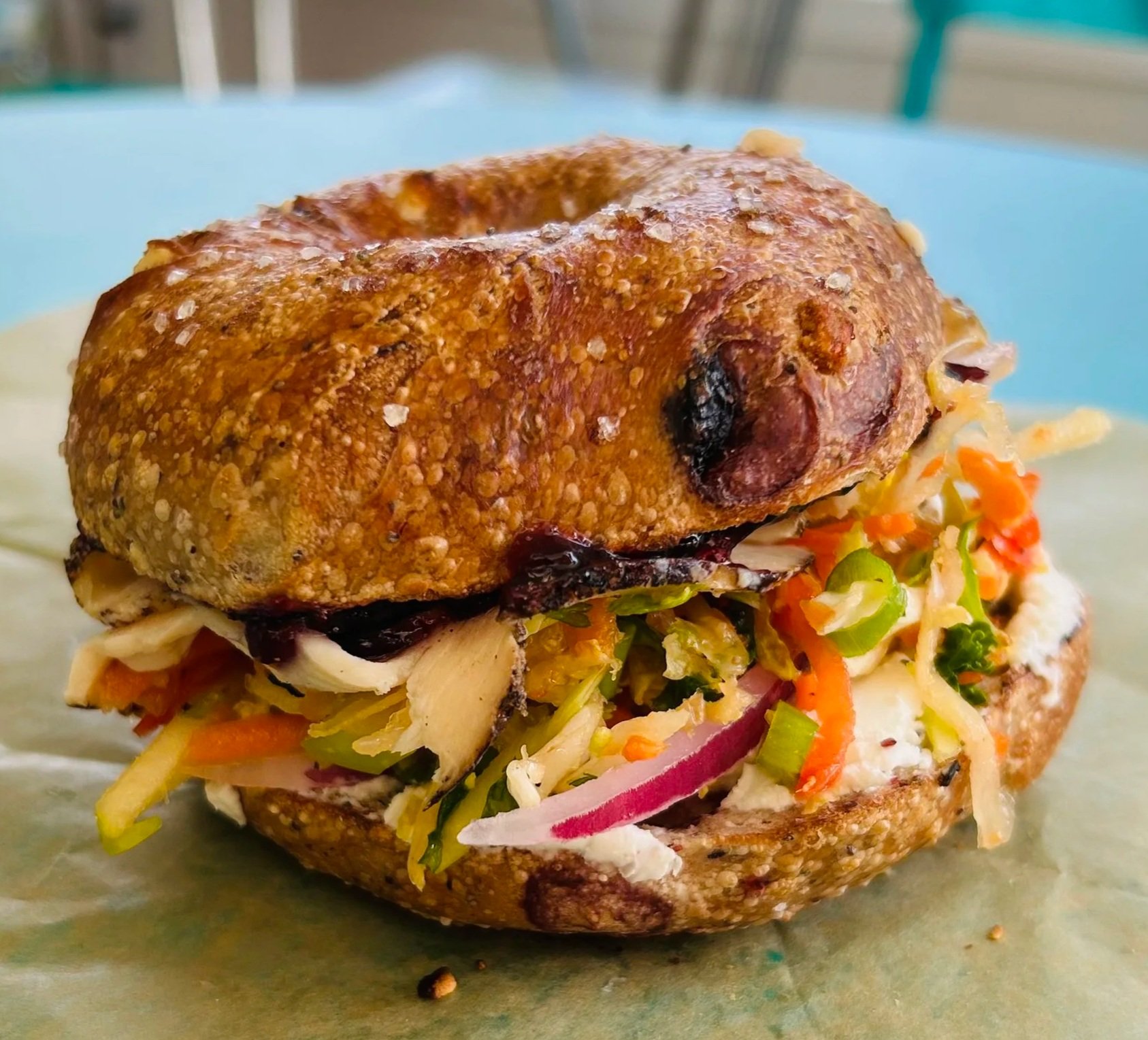 Close-up of a toasted sandwich with various vegetables and chicken, served on parchment paper.