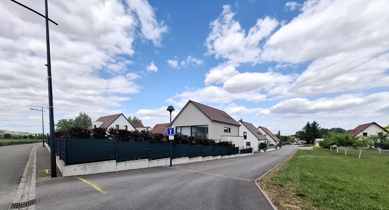 Quartier résidentiel avec des maisons modernes, un ciel partiellement nuageux, un éclairage public et un chemin goudronné.