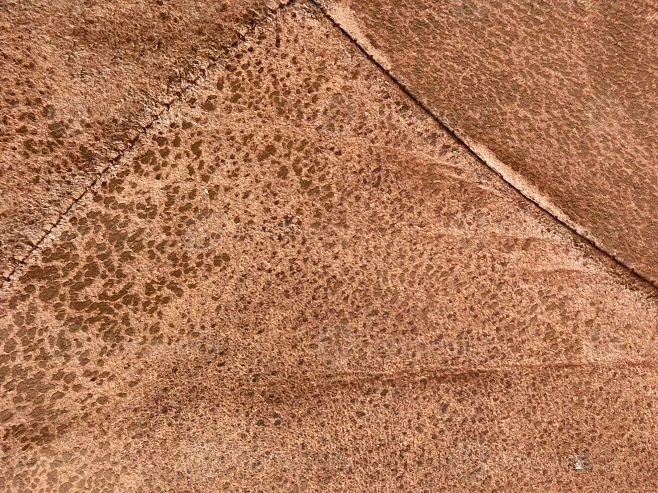 Close-up van een oud stuk leer met een hoek en zichtbaar textuur, stiksel en patina.