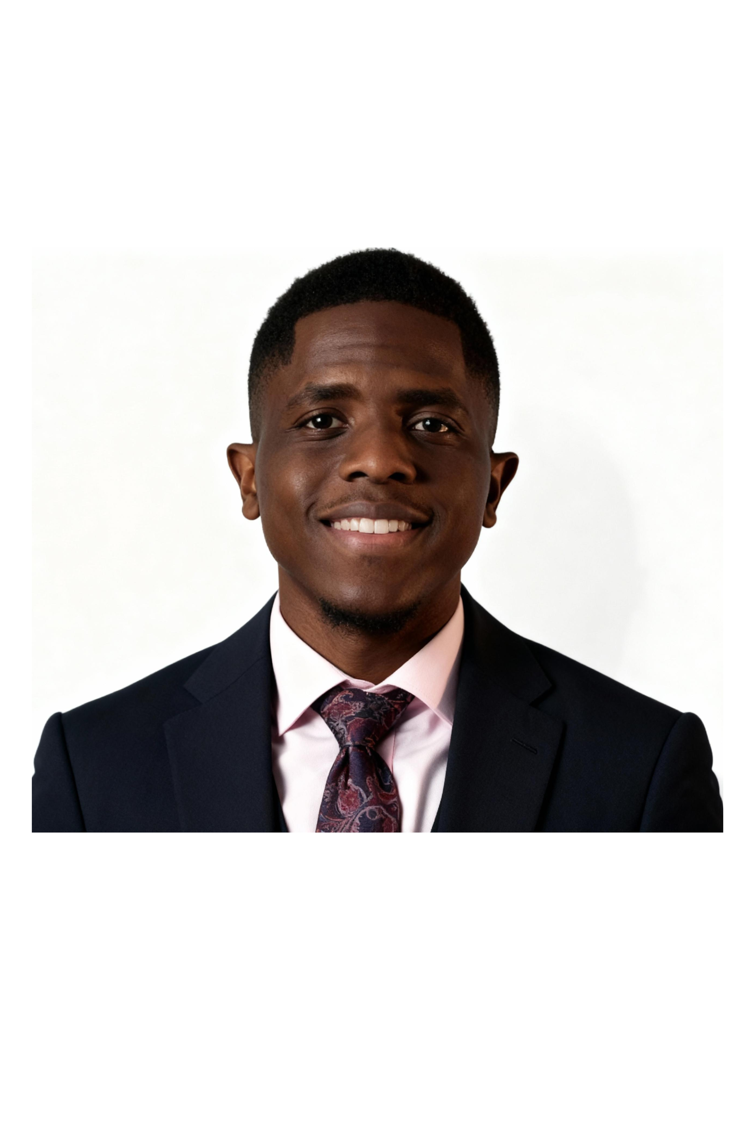 Portrait of a young Black man in a dark suit, light pink shirt, and patterned tie, smiling against a white background.