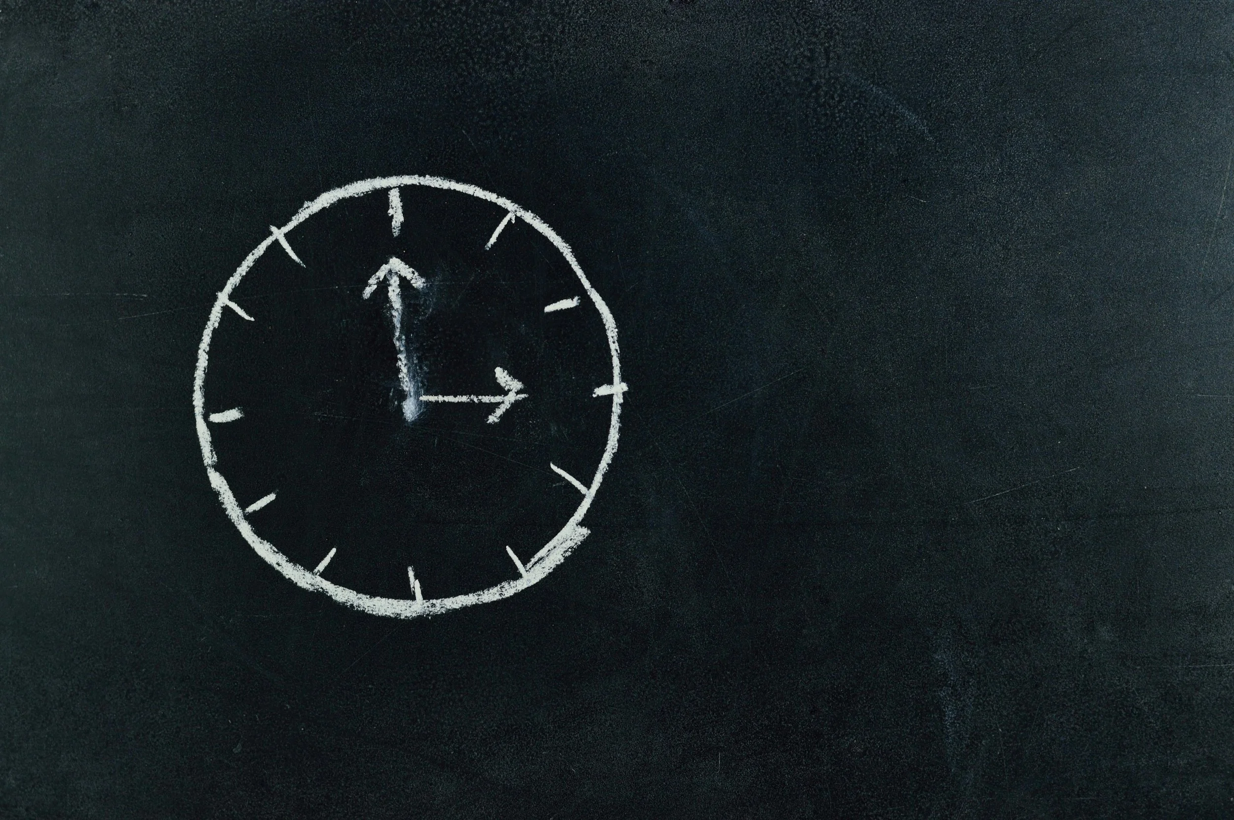 A clock drawn with white chalk on a blackboard, showing the time as 12:15.