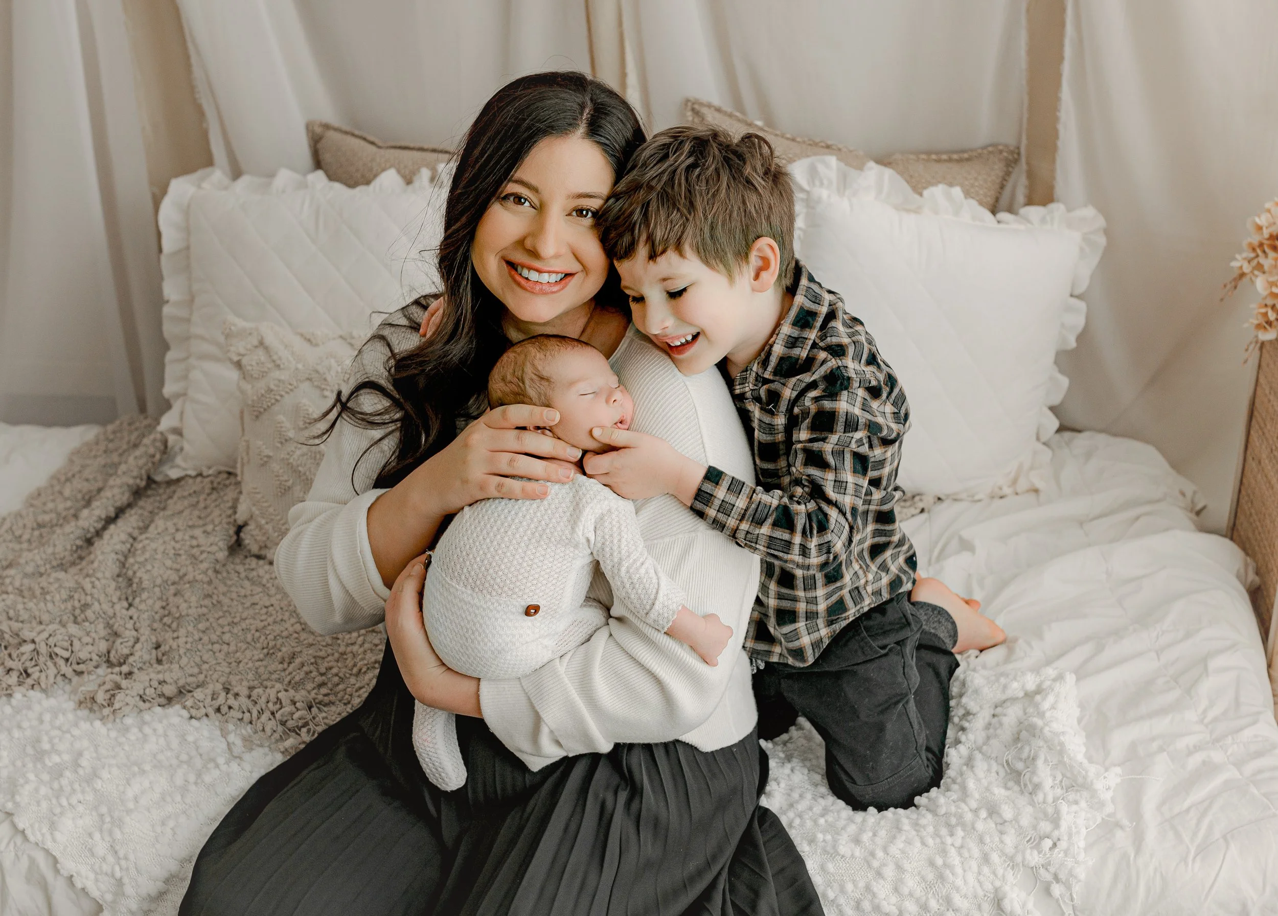 Mom holding newborn with older sibling standing beside them during in-studio session in Round Rock, TX