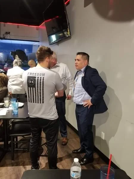 Ben Ruiz speaking with a constituent at a restaurant or bar, with other people in the background and a TV on the wall.