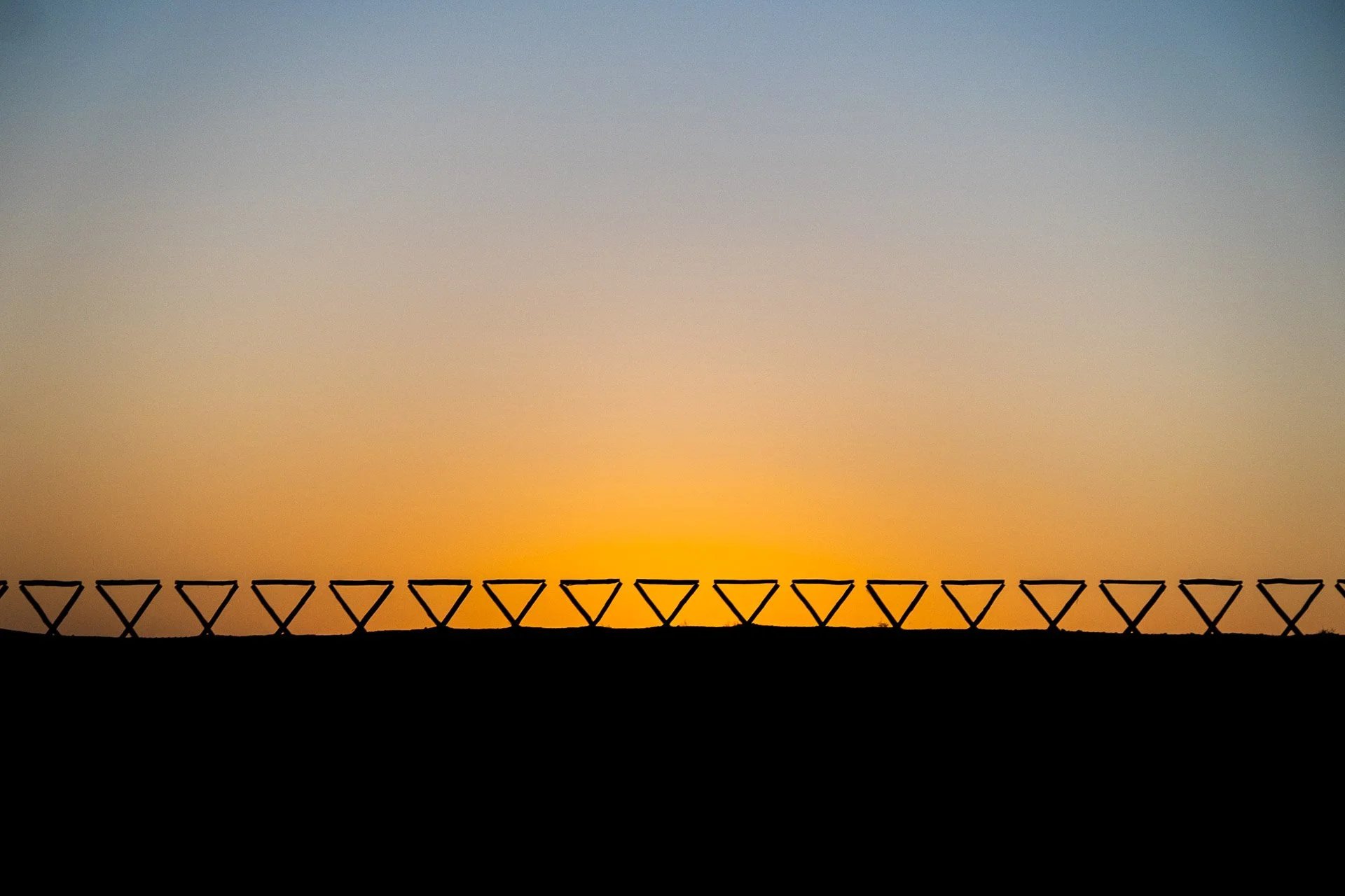 Silhouette of solar panels against a sunrise or sunset sky with a gradient of blue to orange.