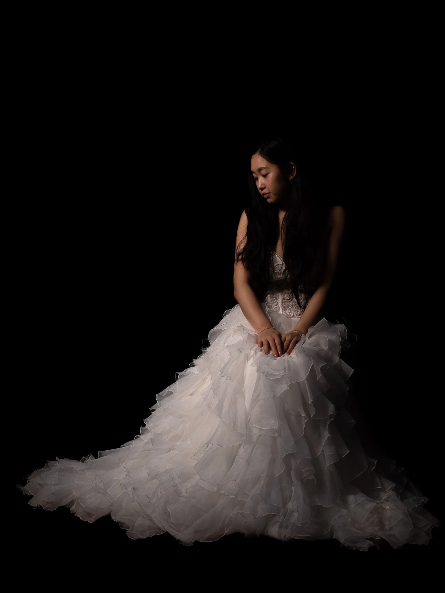 Young woman in a white wedding gown sitting against a black background.