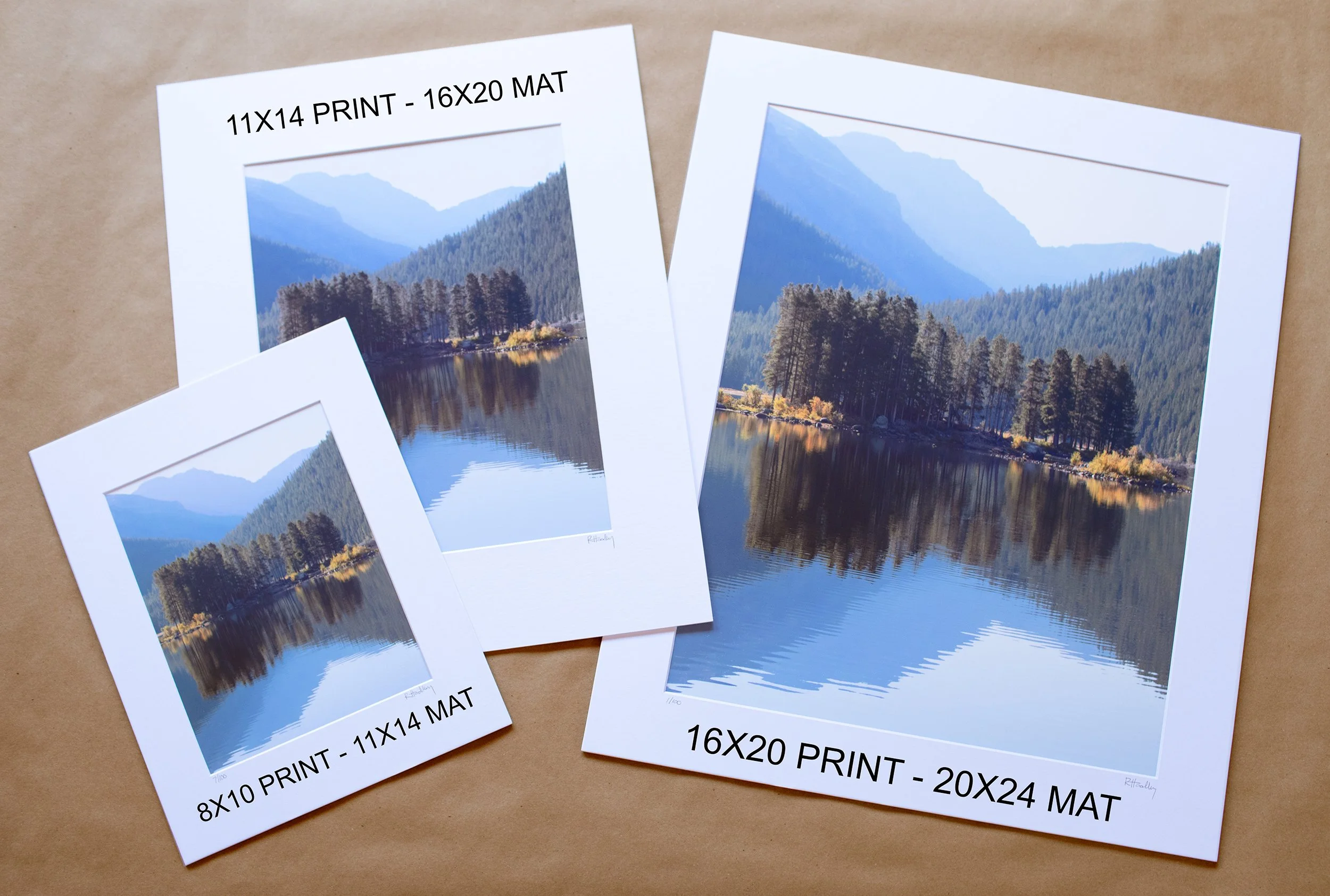 Three prints of a landscape scene depicting a calm lake with trees along the shoreline, surrounding mountains, and a partly cloudy sky, with the sizes labeled as 8x10, 11x14, and 16x20 inches.