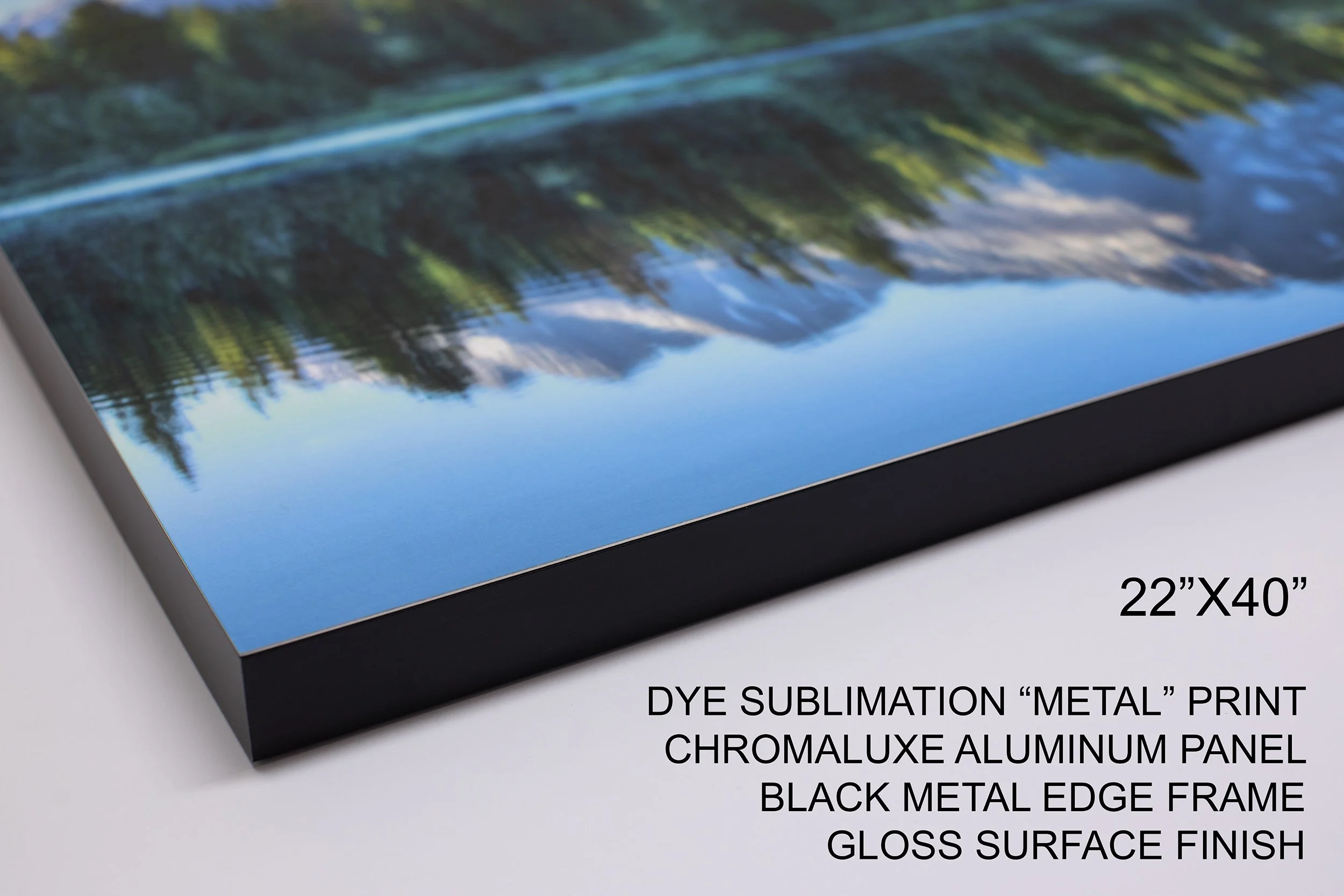 Close-up of a chromaluxe aluminum print featuring a scenic landscape of mountains, trees, and a lake, with black metal edge frame and gloss surface finish, measuring 22 inches by 40 inches.