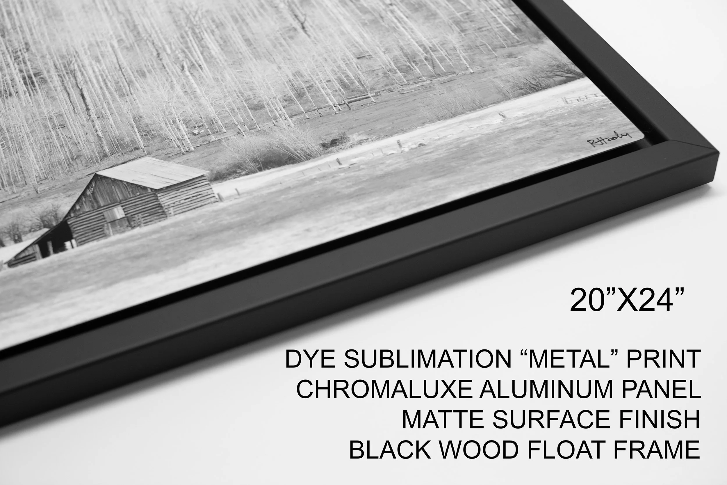 A black aluminum picture frame with matte surface finish, displaying a black-and-white landscape photograph of a barn and trees, with a white background and product specifications including size 20 inches by 24 inches and a dye sublimation metal print.